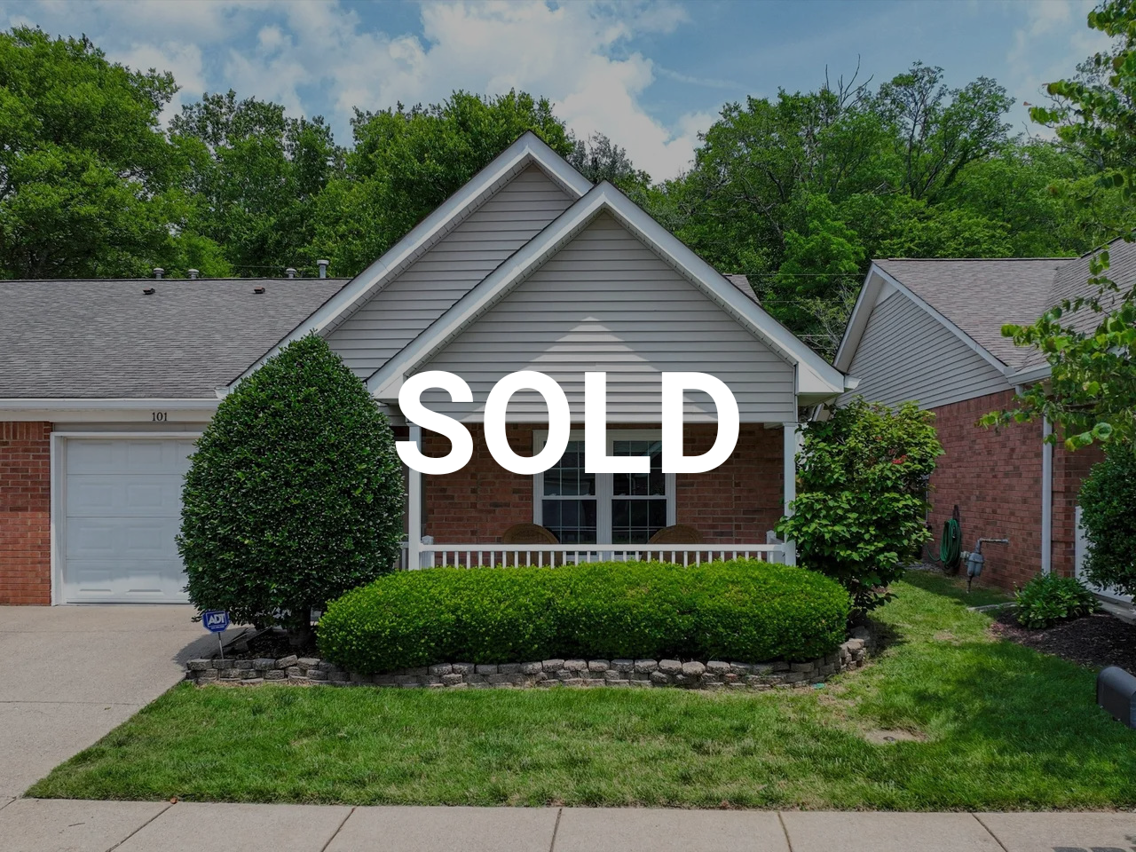 Front view of a house with a brick facade, gray roof, and green bushes in the garden. The house has a porch and the word SOLD is overlaid in white letters.