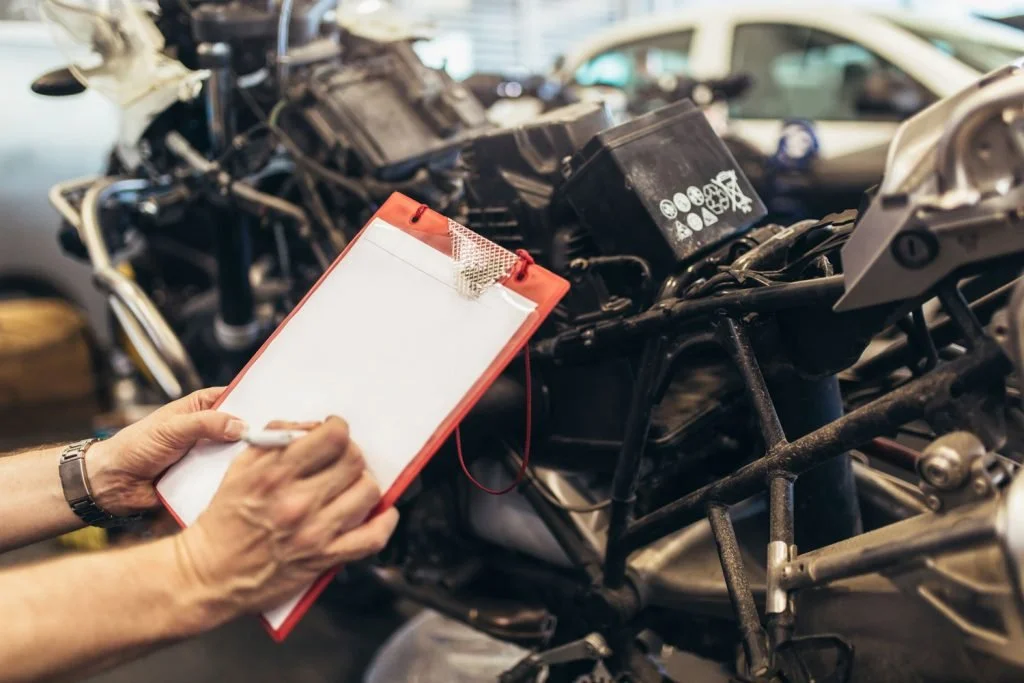 Person taking notes on a clipboard while inspecting a damaged car frame.