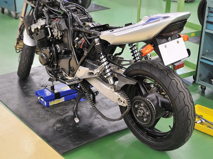 A motorcycle being repaired or assembled in a workshop, with the seat and body panels removed, revealing the engine and internal components.