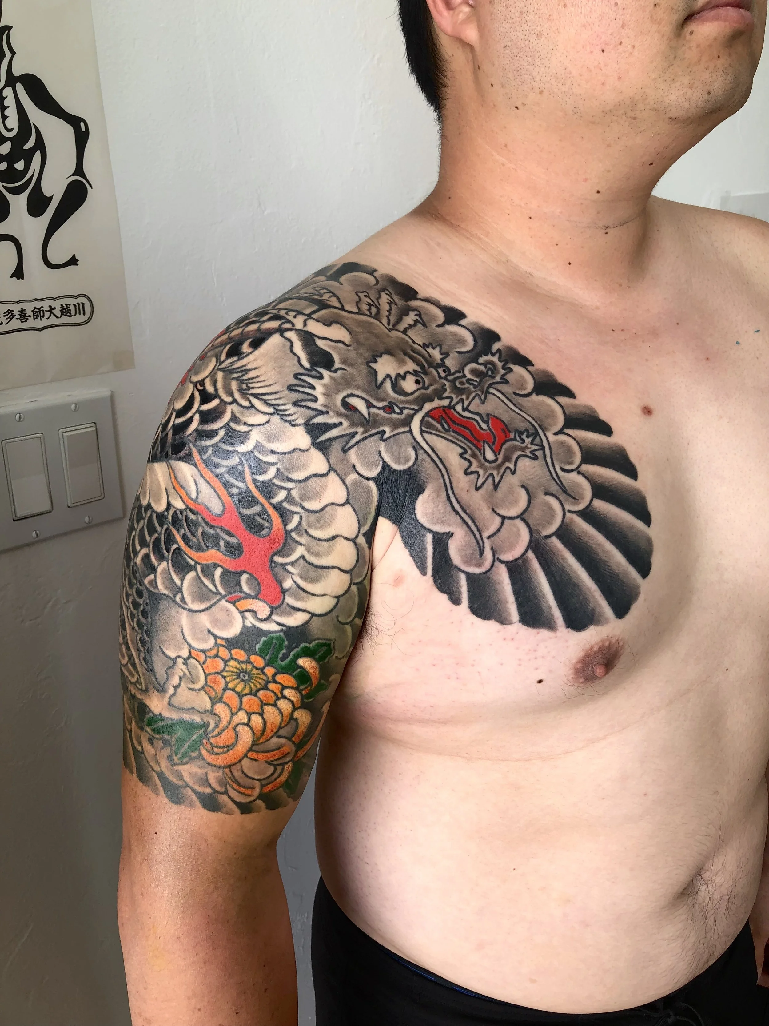 A man with a detailed traditional Japanese-style colorful tattoo on his shoulder and upper arm, featuring a dragon and various other decorative elements.