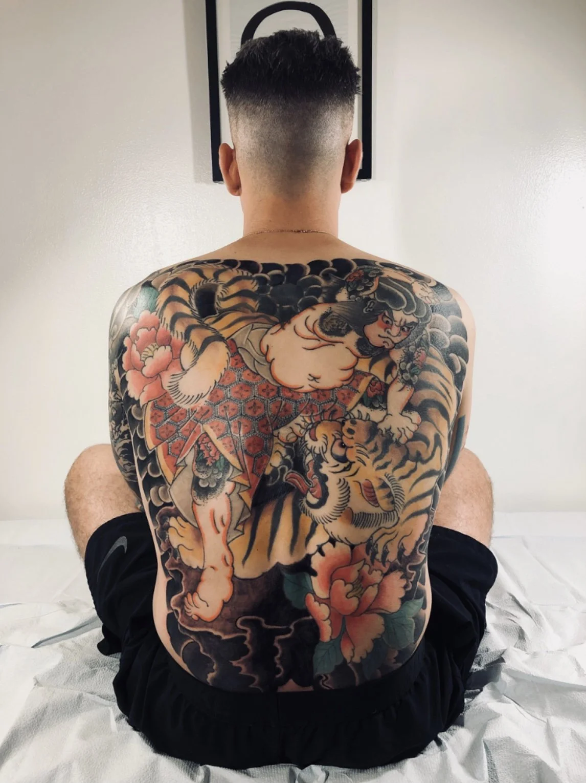 A person with a heavily tattooed back featuring traditional Japanese-style artwork of a sumo wrestler and a tiger.