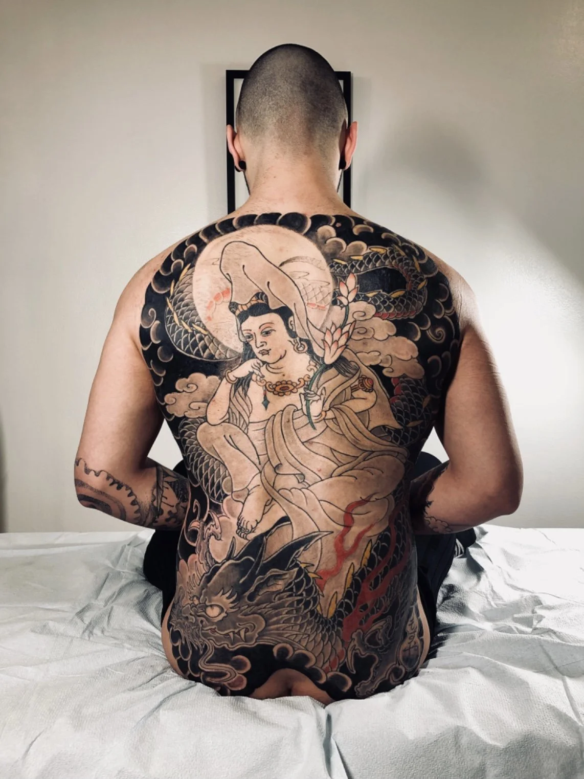 Back view of a person with a large traditional Japanese style tattoo on their back, depicting a woman, a dragon, and clouds.