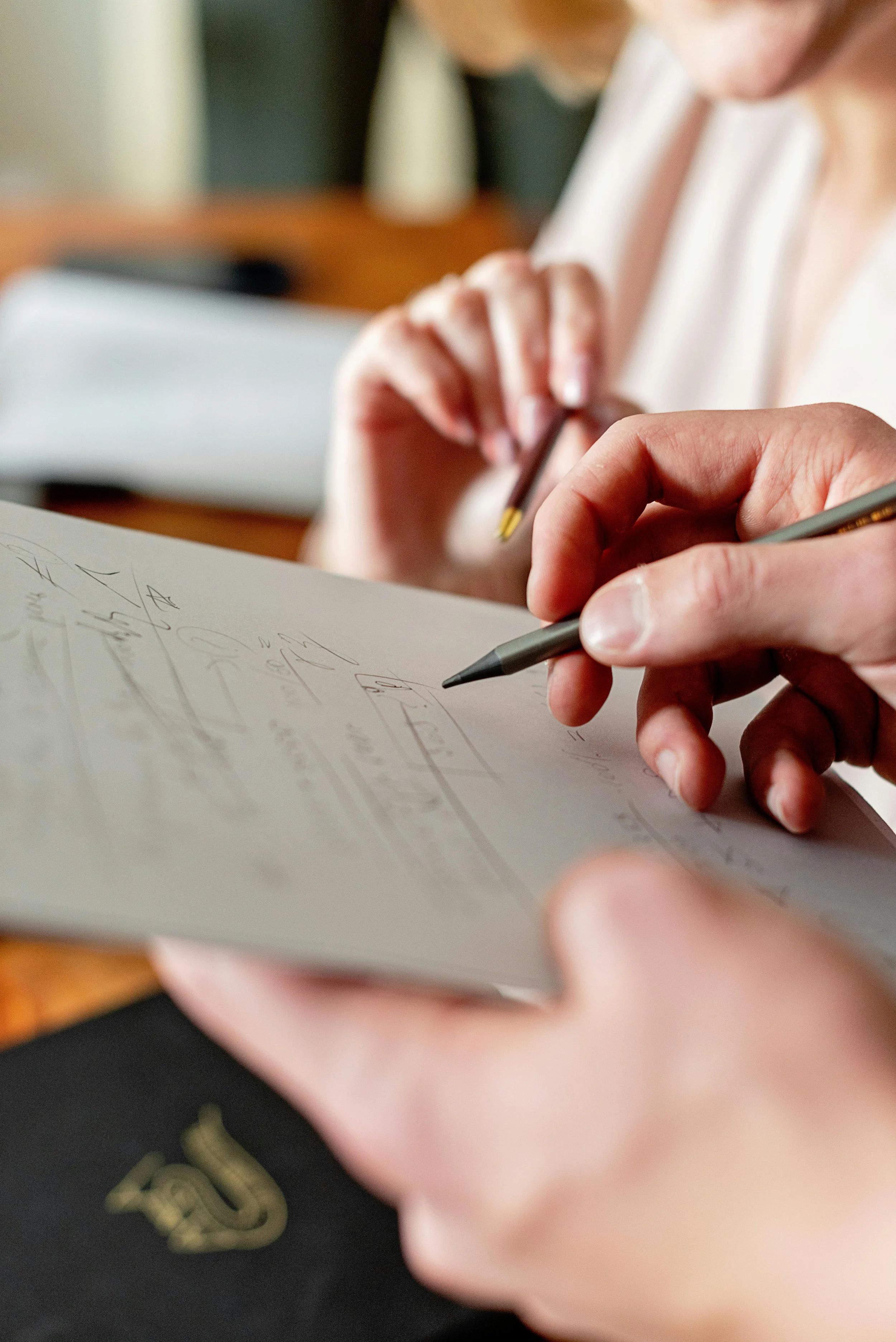 Close-up of a person holding a pen and writing or drawing on a piece of paper or notebook.