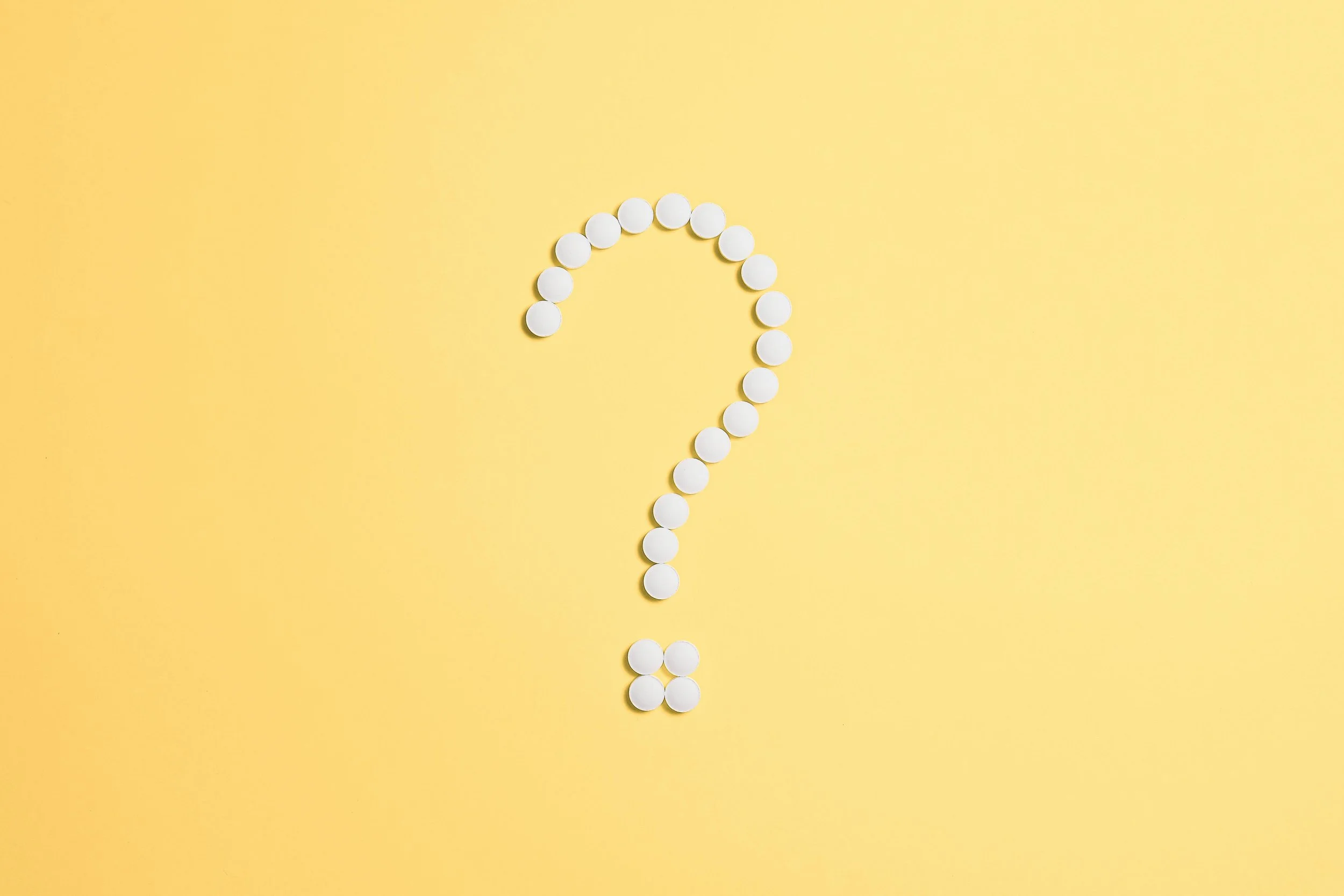 A yellow background with white pills arranged in the shape of a question mark.