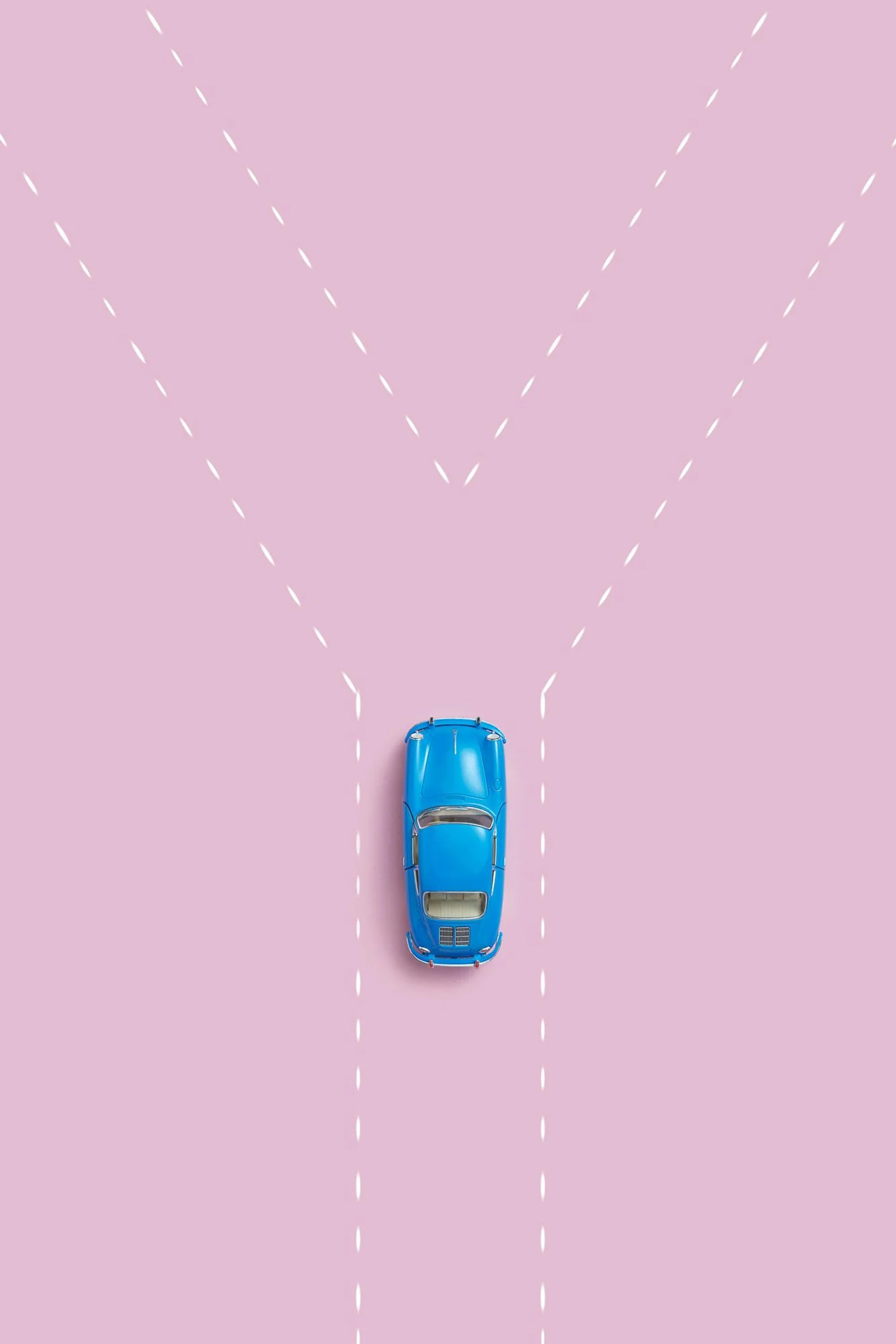 A blue toy car sits at a Y‑shaped intersection marked with white dashed lines on a pink background, representing a moment of choosing between two paths.