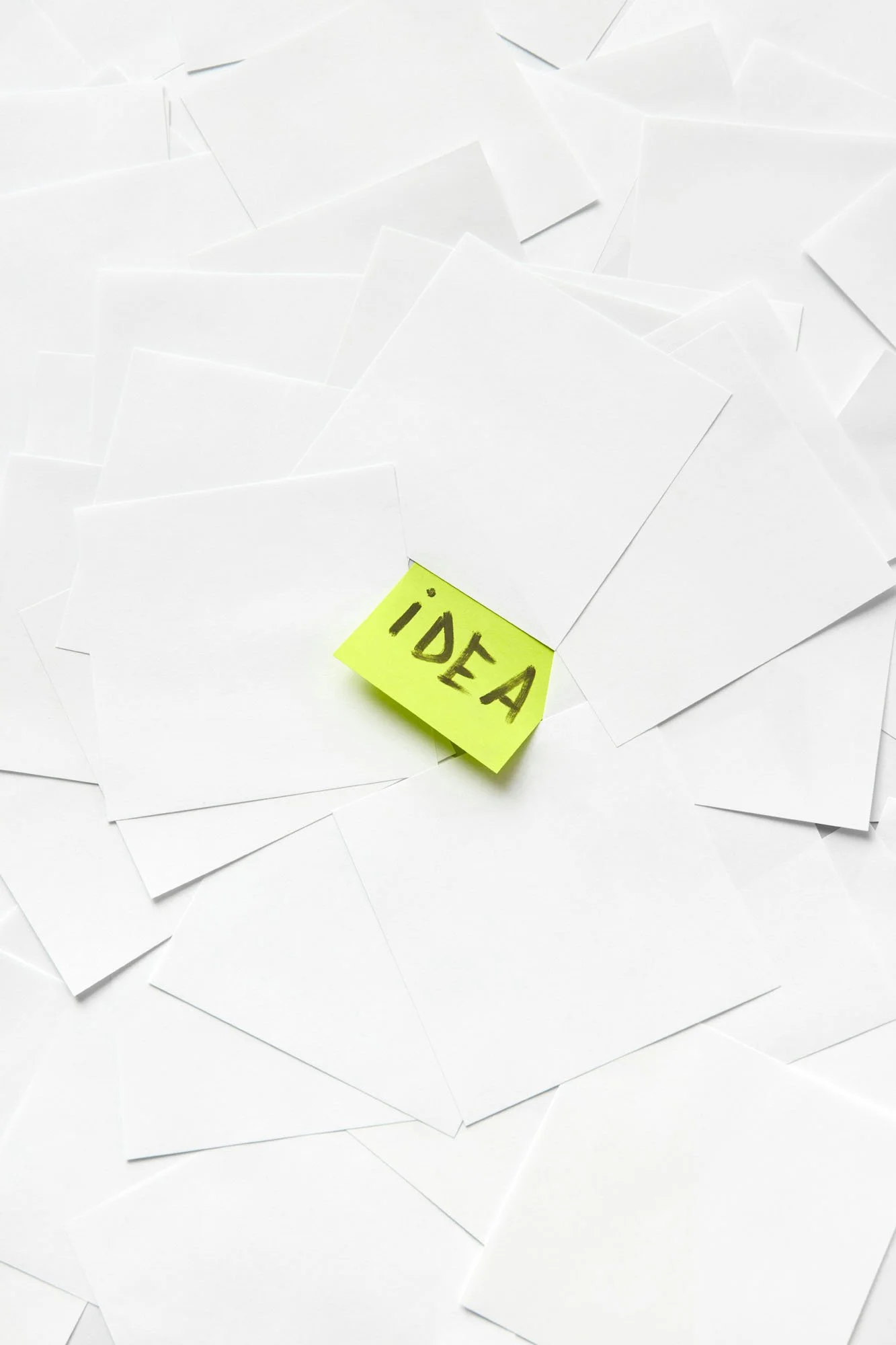 A yellow‑green sticky note with the word ‘IDEA’ written in bold black letters placed on top of scattered white sheets of paper.