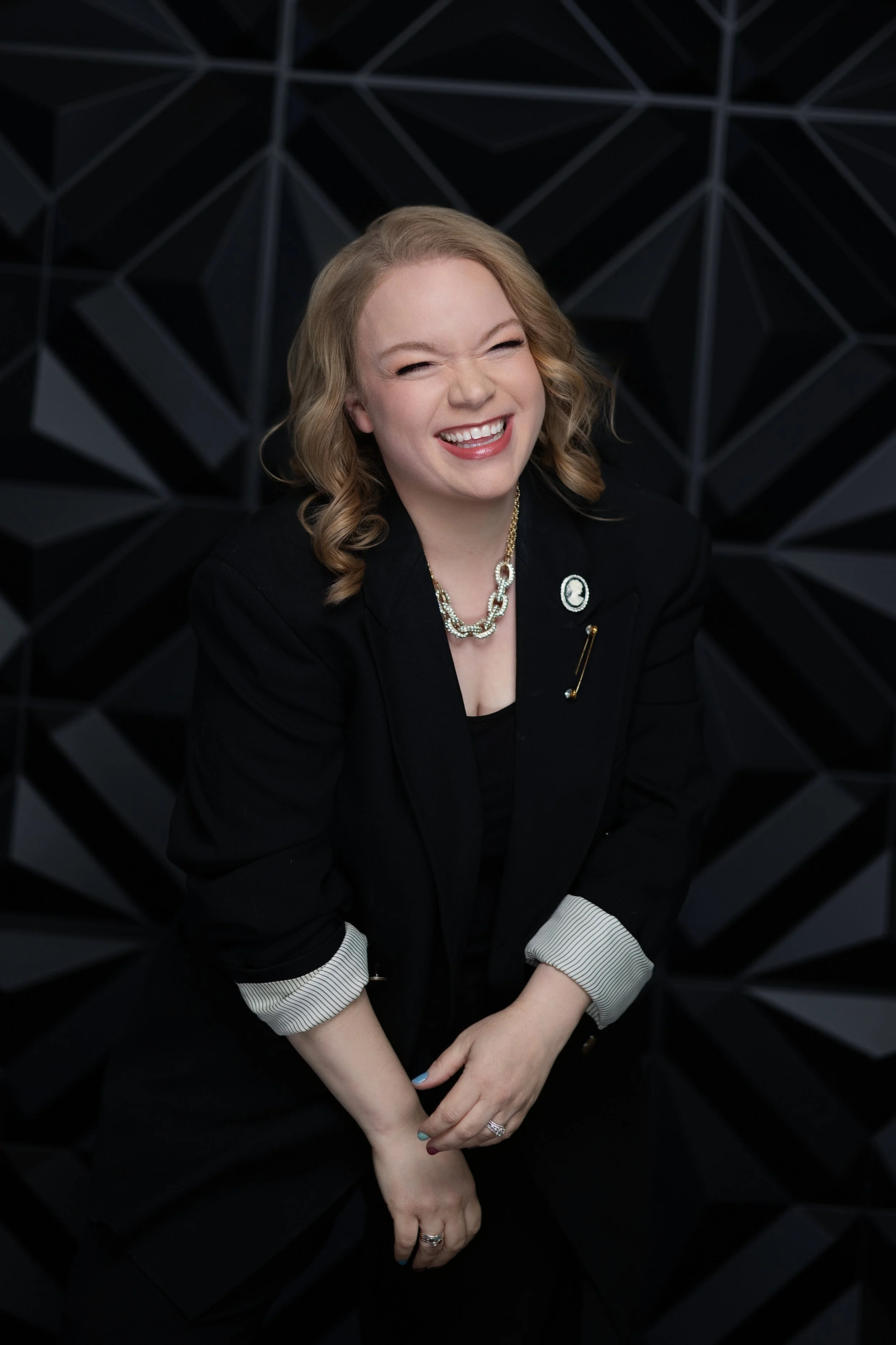 Jessie Hemmelgarn wearing a black blazer and jewelry, sitting against a geometric black background.