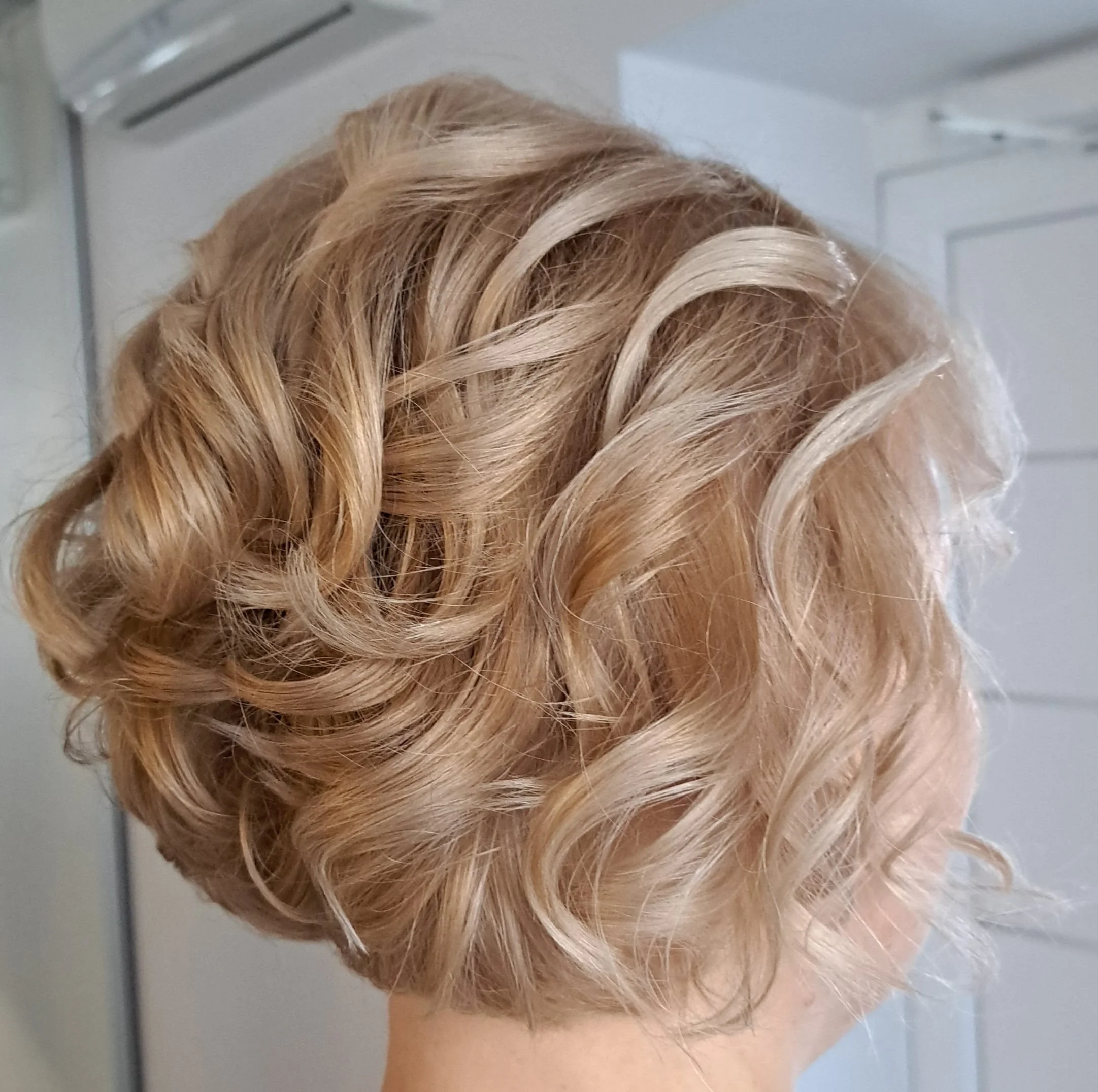 Trumpų šviesių garbanotų plaukų kirpimas salone „Edita“.