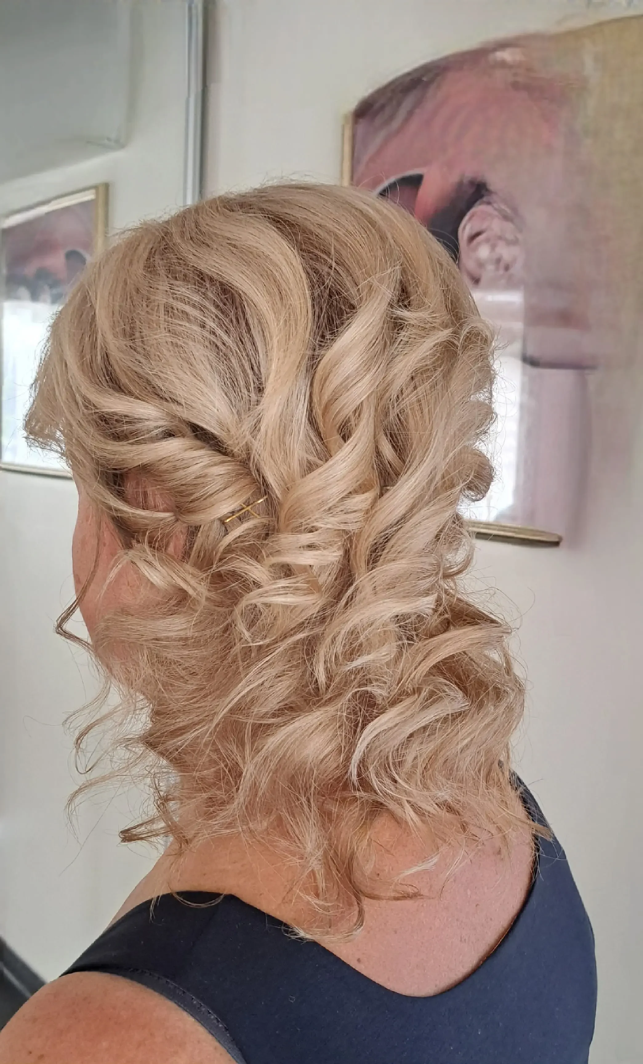 Šviesių garbanotų plaukų šukuosena su auksiniu segtuku salone „Edita“.