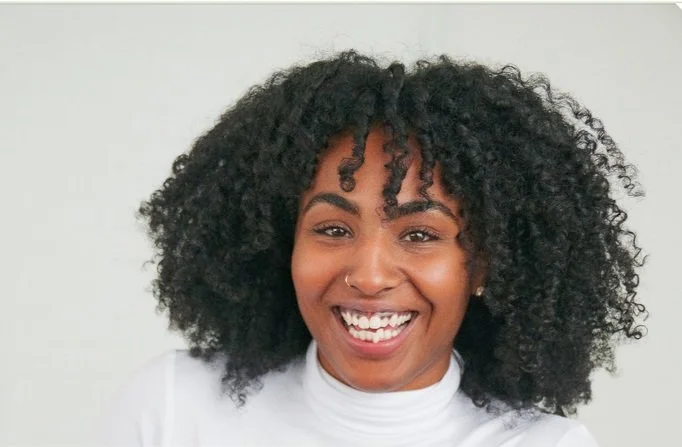 A woman with dark, curly hair smiling at the camera.