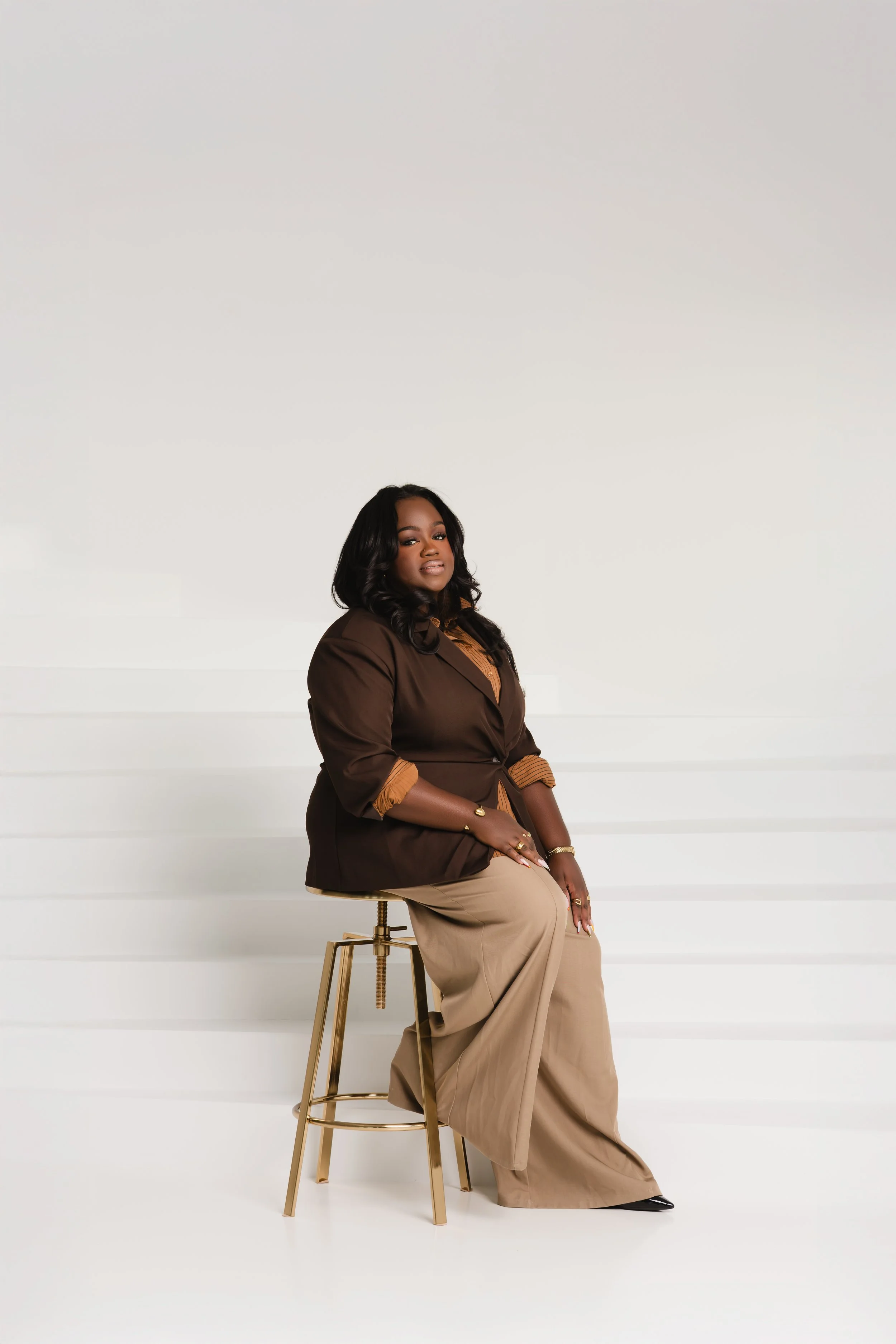 Ayanna, founder of Ayanna Design Studio, seated in a brown blazer and neutral trousers.
