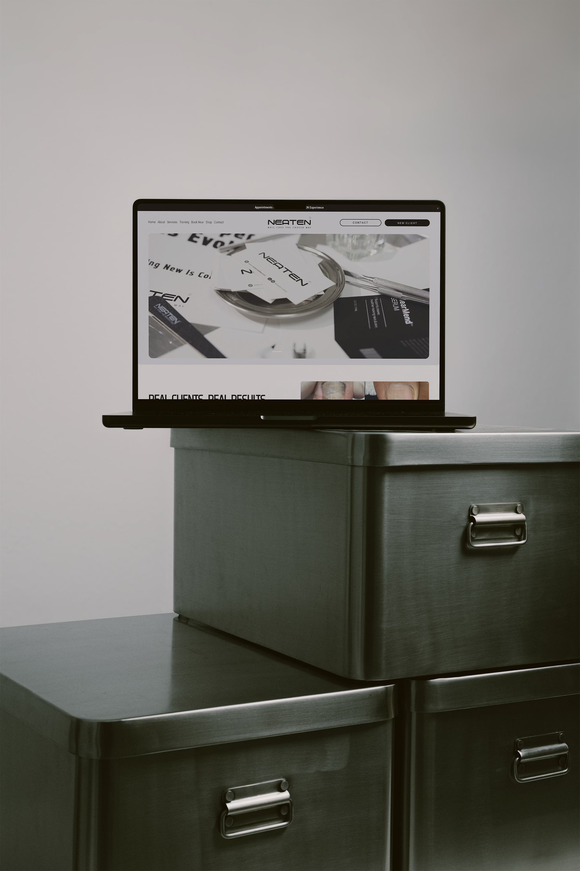 A laptop on top of a metal filing cabinet displaying a website for a nail care business named Neaten, with images of nail designs and related advertisements.