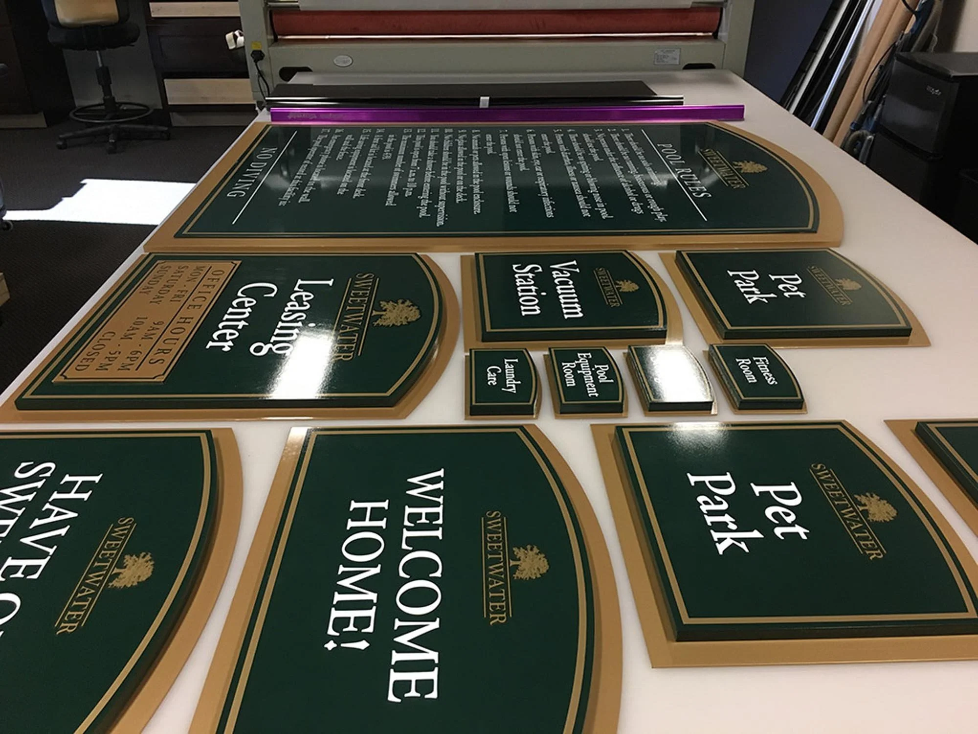 Various green and gold signboards for a winery, including signs for tasting station, pet park, and restrooms.