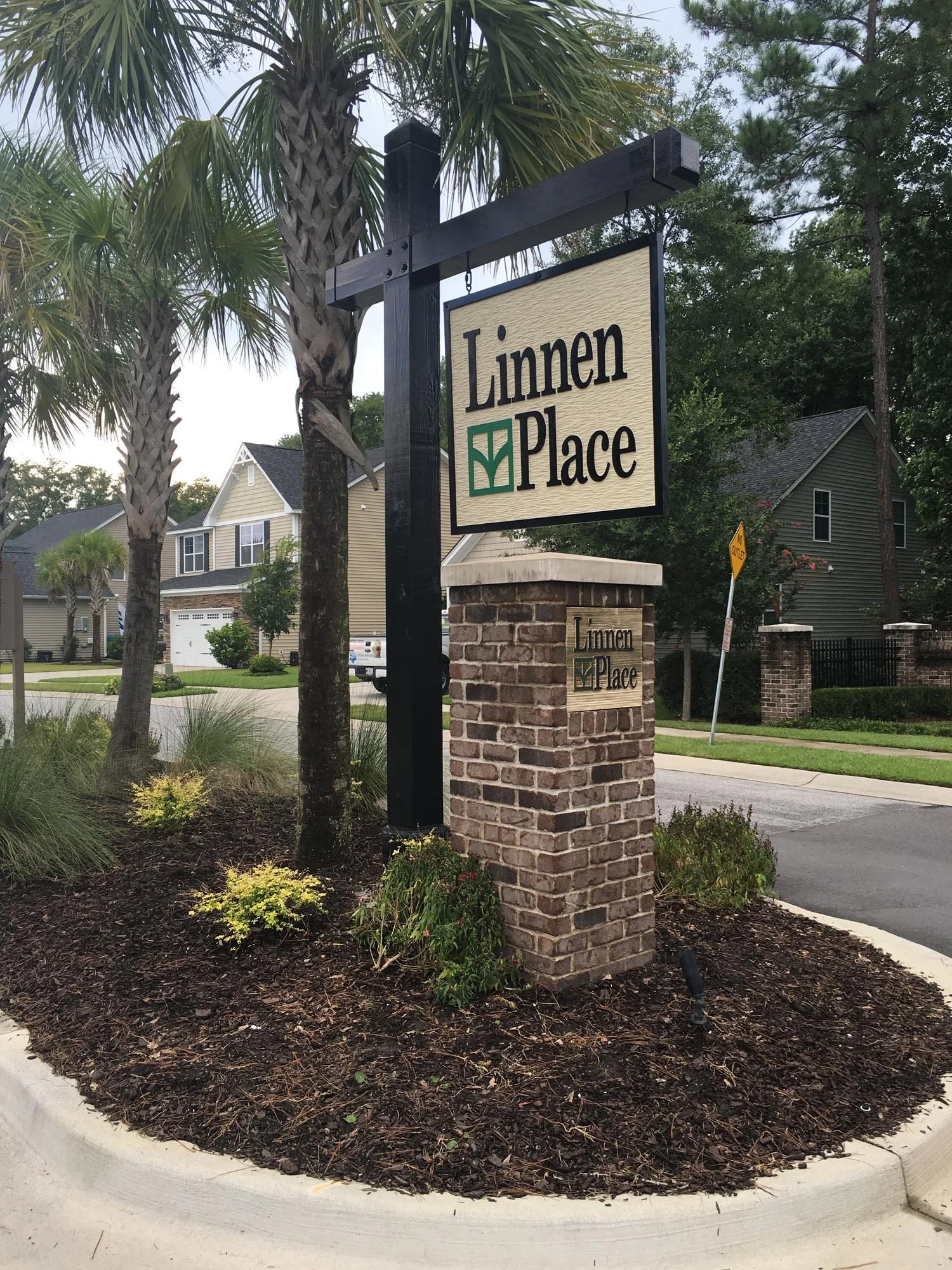 Sign reading 'Linnen Place' attached to a brick pillar near palm trees and residential houses.