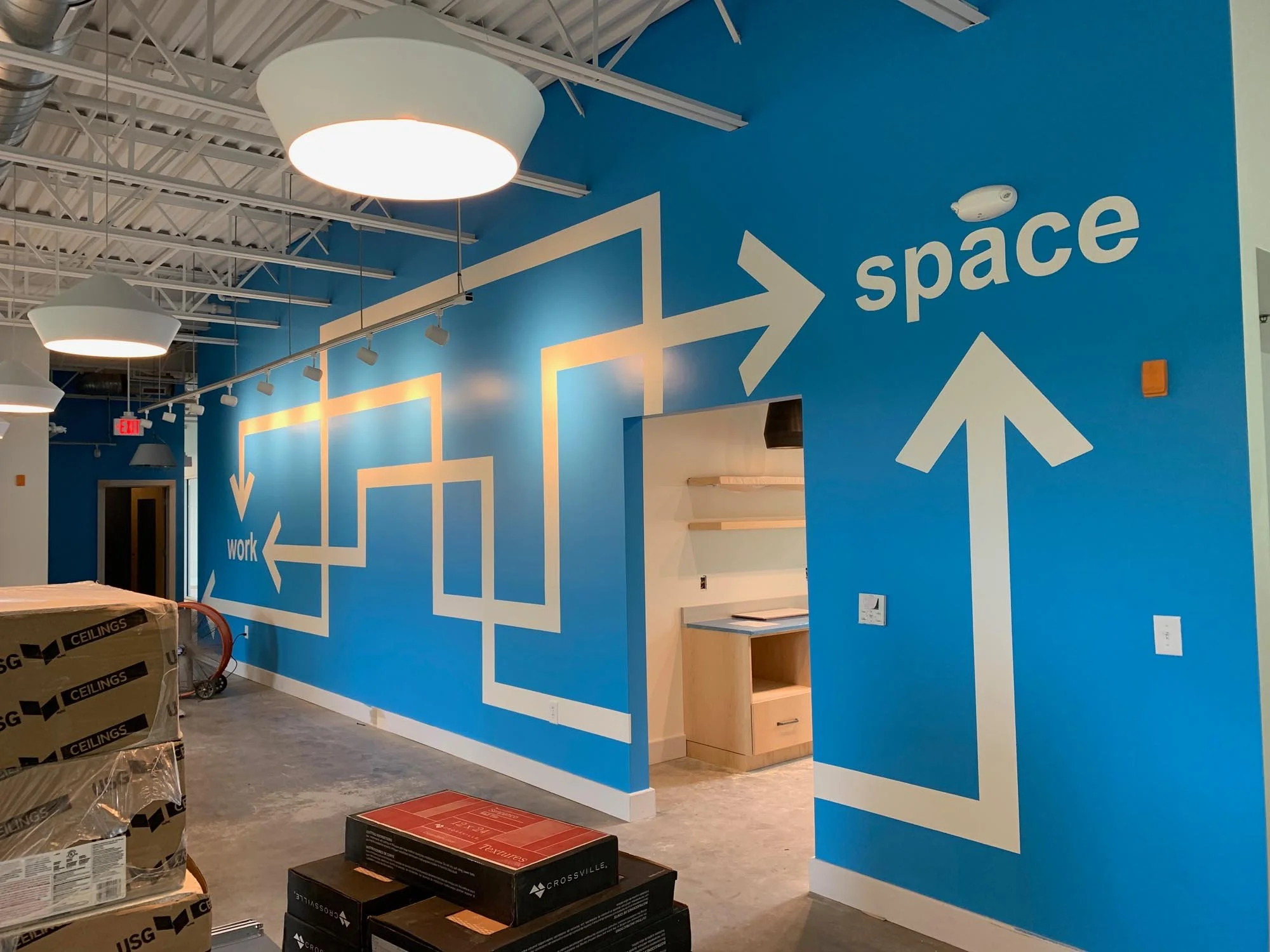 Blue wall with white directional signage pointing to space and work areas, including arrows and text, in a modern office or studio space under construction.
