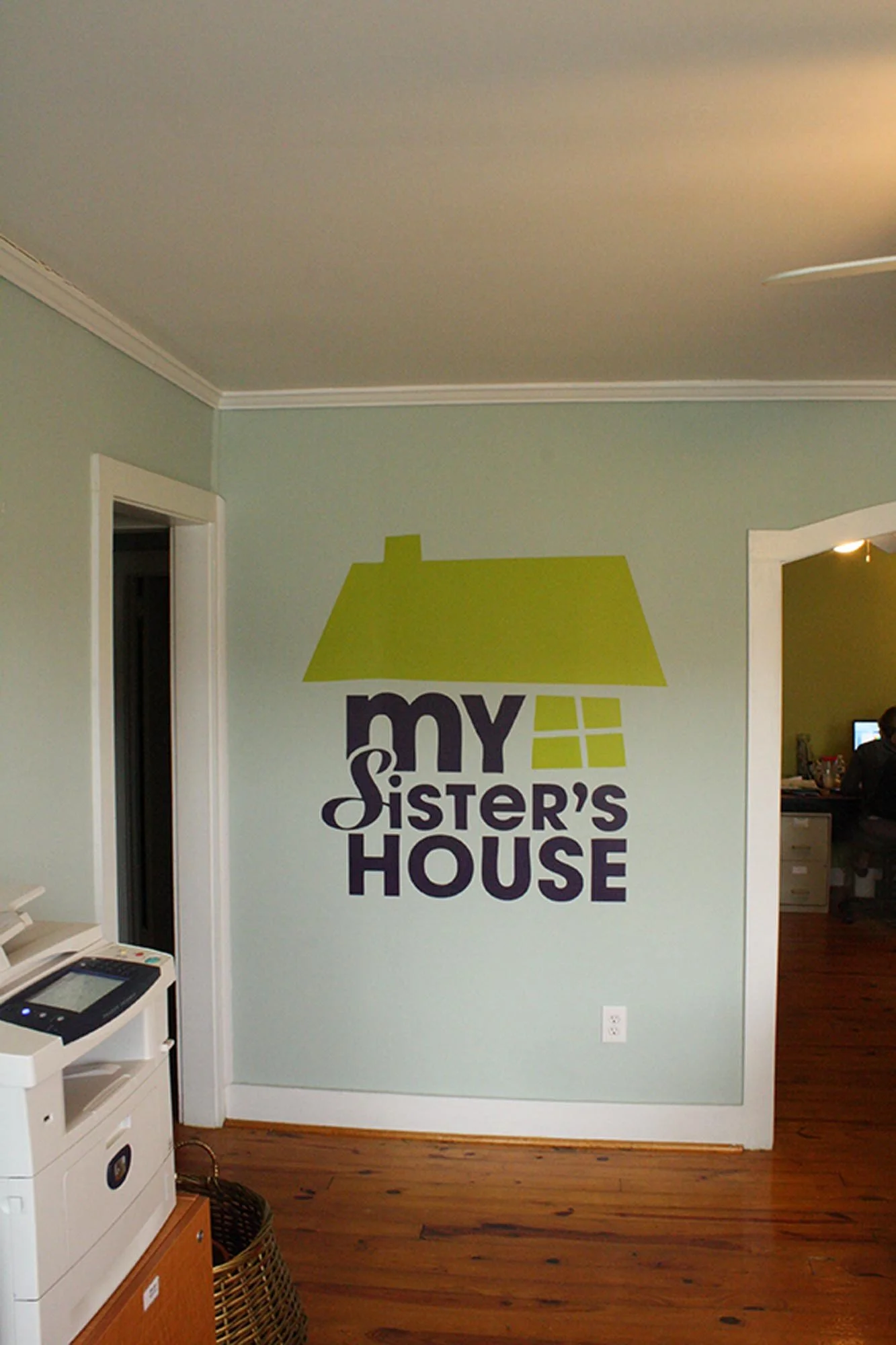 Wall decal with a green house roof and a window design, alongside the text "my sister's house" in purple letters.