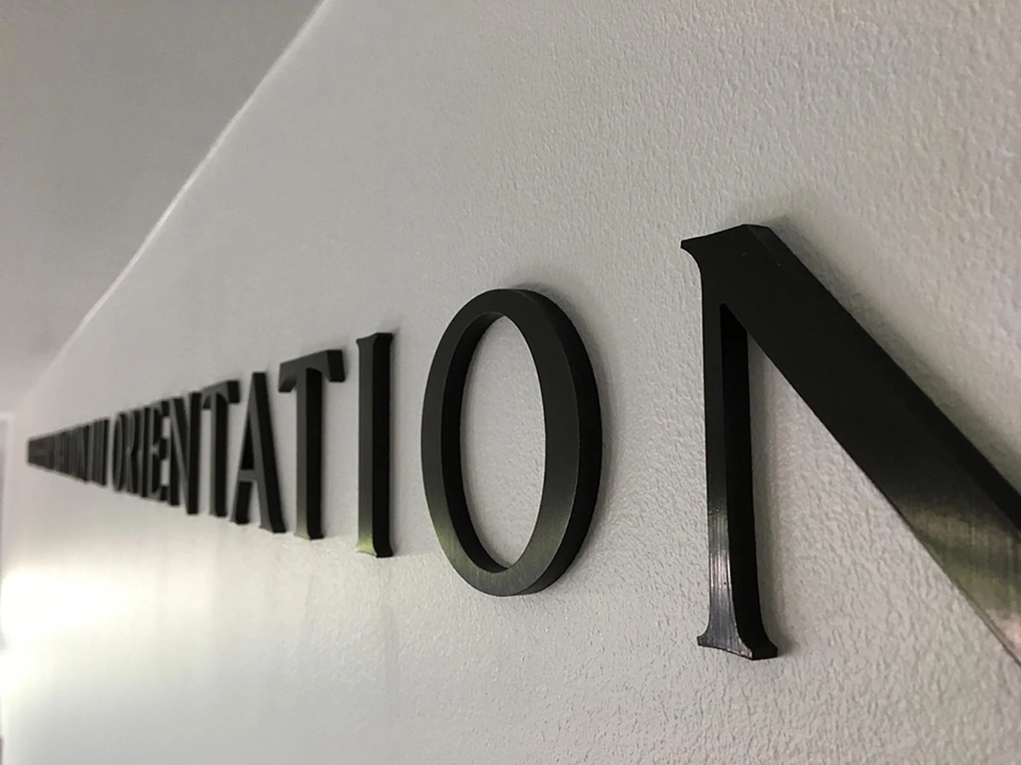 Close-up of black 3D letters on a wall spelling "O" and part of a word beginning with "D".