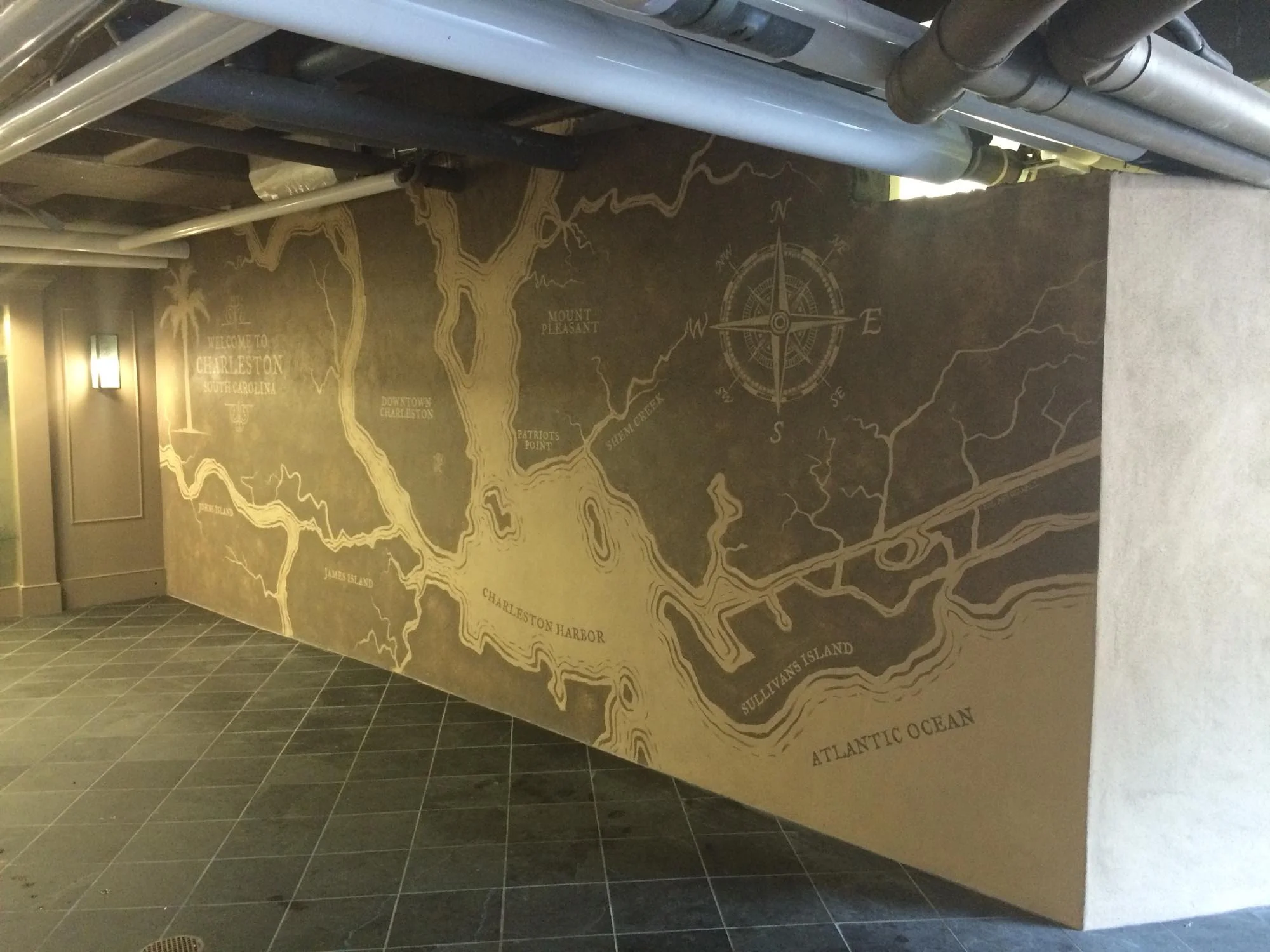 Wall mural of a map of Charleston, South Carolina, including landmarks like Charleston Harbor, Sullivan's Island, and the Atlantic Ocean, with a compass rose and street names.