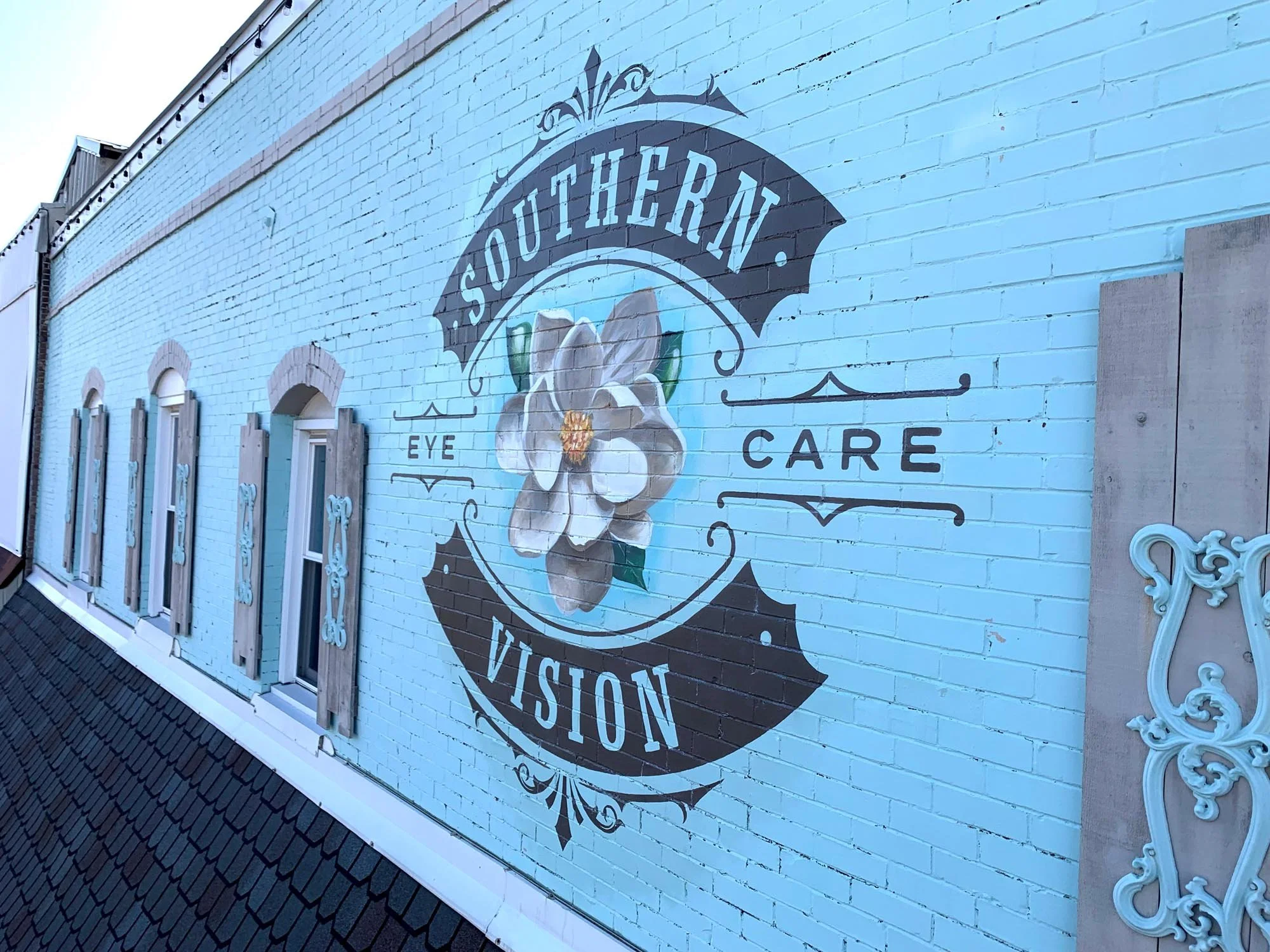 Exterior brick wall painted with a mural for Southern Vision Eye Care featuring a magnolia flower and ornate decorative elements.