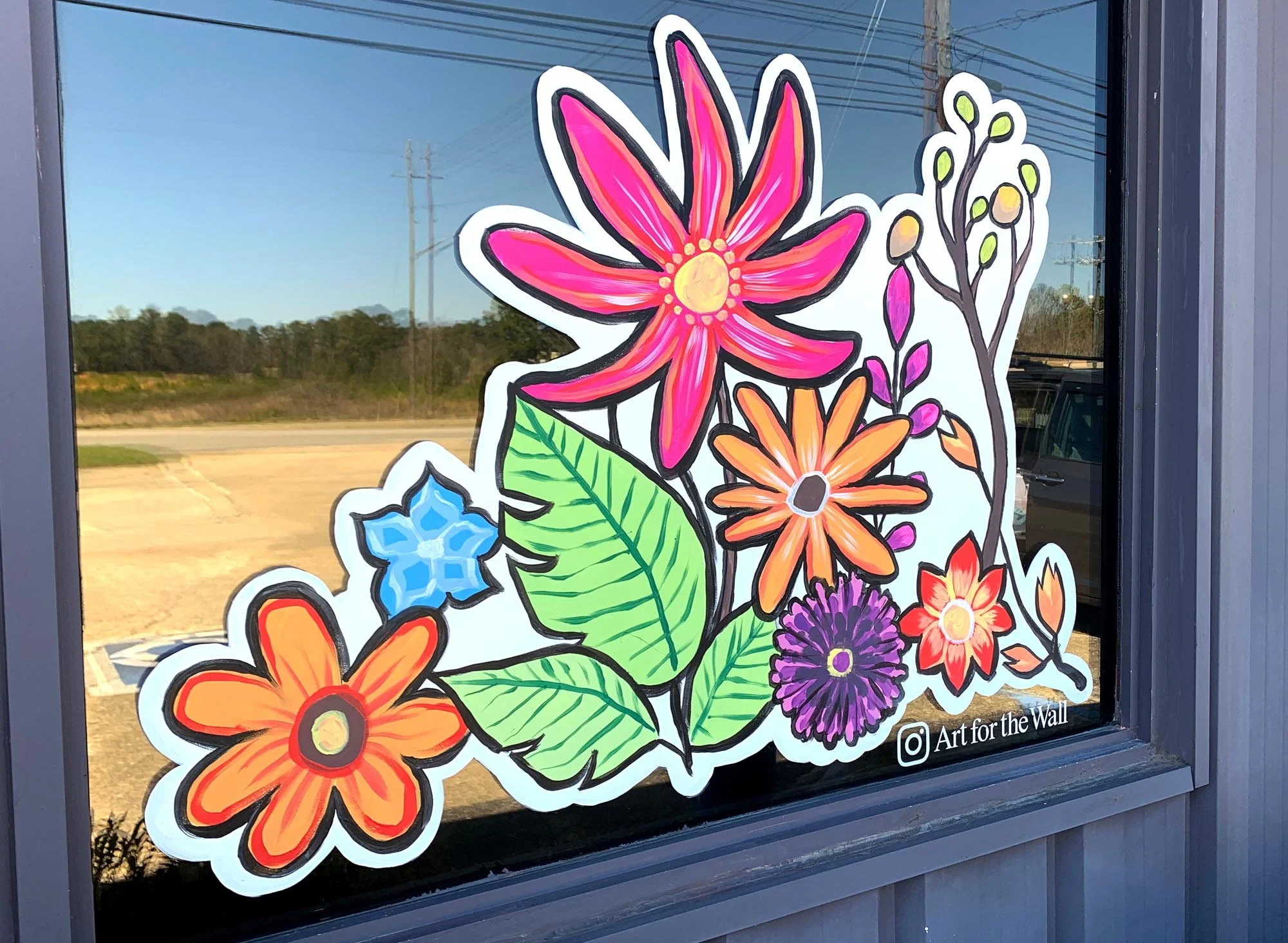 Colorful floral sticker with pink, orange, purple, and blue flowers and green leaves on a window, with a reflection of the outdoors.