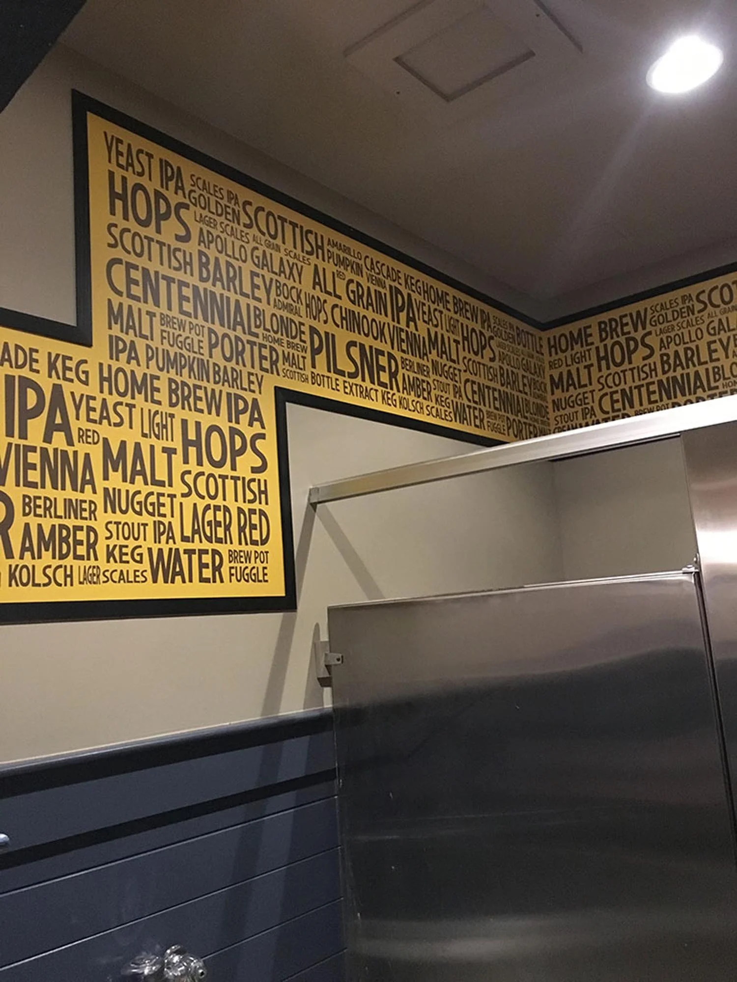 Interior of a brewery or pub with walls decorated with words related to beer styles, ingredients, and brewing terms in yellow and black colors.