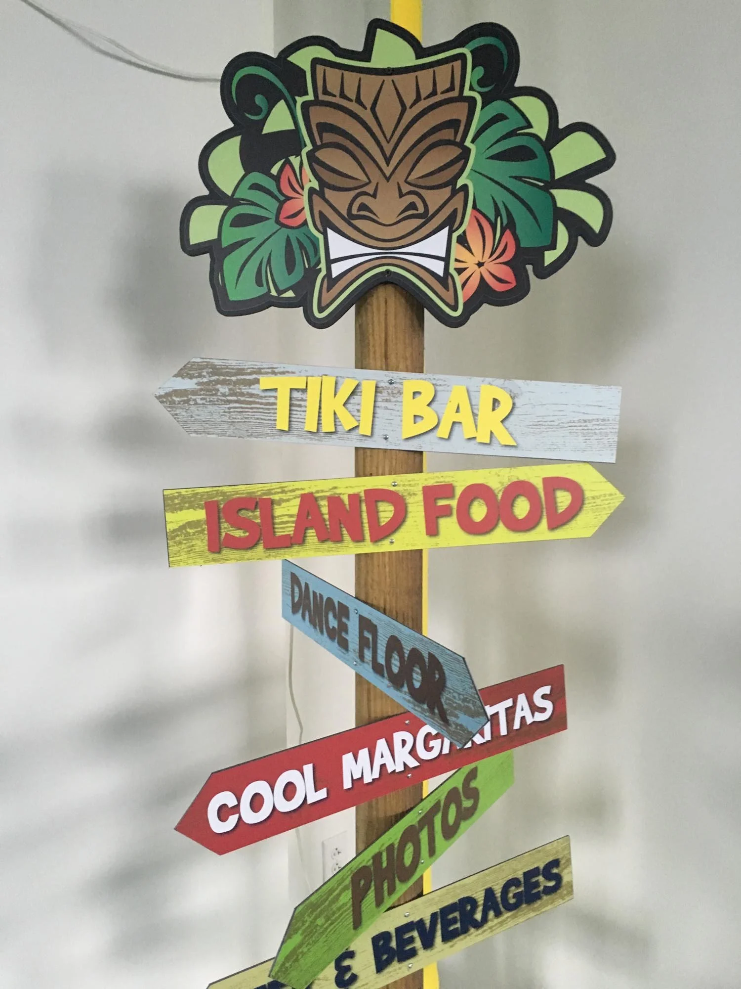 Colorful signpost with tropical island-themed decorations at the top, pointing to various destinations including Tiki Bar, Island Food, Dance Floor, Cool Margaritas, Photos, and Beverages.