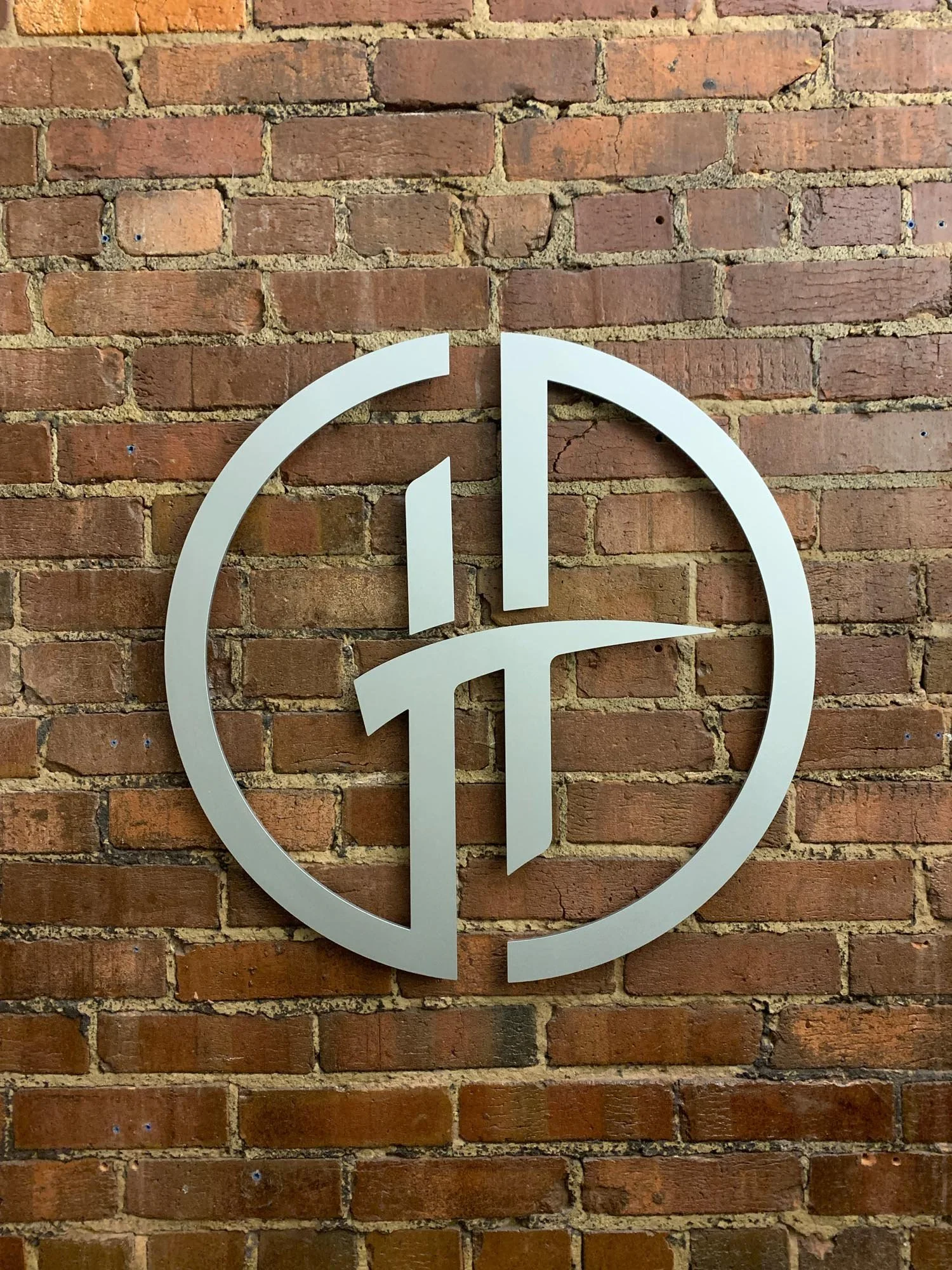 Modern metal sign with a circular design and geometric lines mounted on a red brick wall.