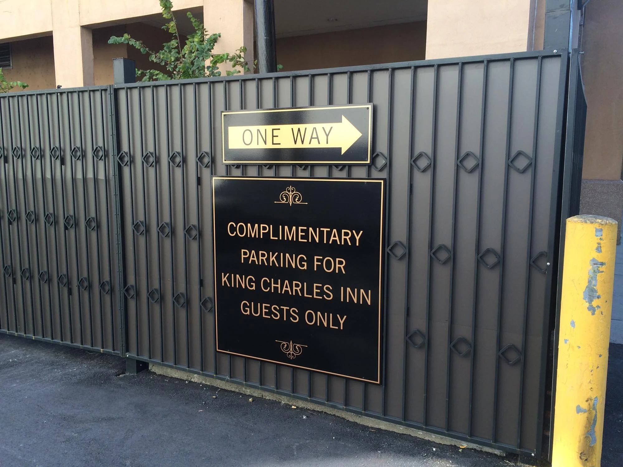 A sign on a metal fence stating 'One Way' with an arrow pointing to the right, and another sign below it reading 'Complimentary Parking for King Charles Inn Guests Only'.