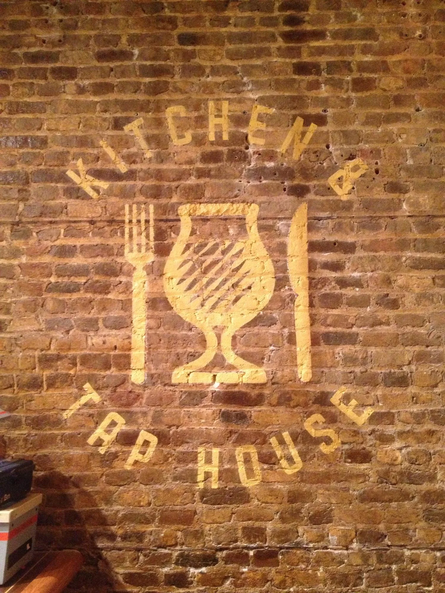 Brick wall with a painted logo of a wine glass, a fork, and the words "WITCHEN & APPETIZERS" arranged around the glass.