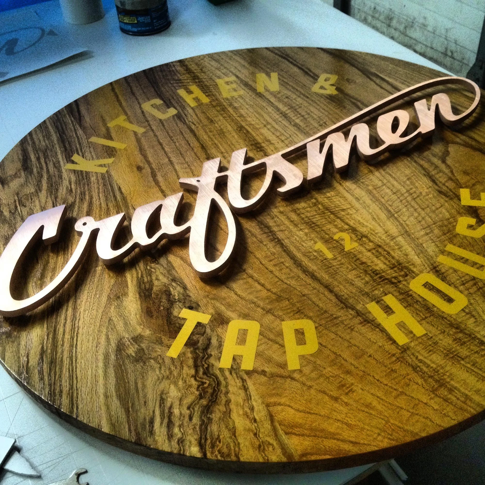 A round wooden sign with the name "Grayton" in large cursive letters in the center, and the words "Kitchen," "TAP," and "HOP" arranged around it.
