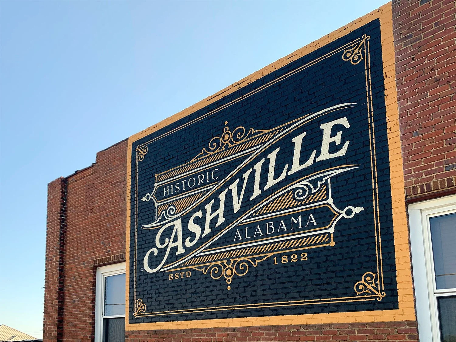 A large mural on the side of a red brick building that reads 'Historic Ashville, Alabama, estd 1822' with decorative borders and design.