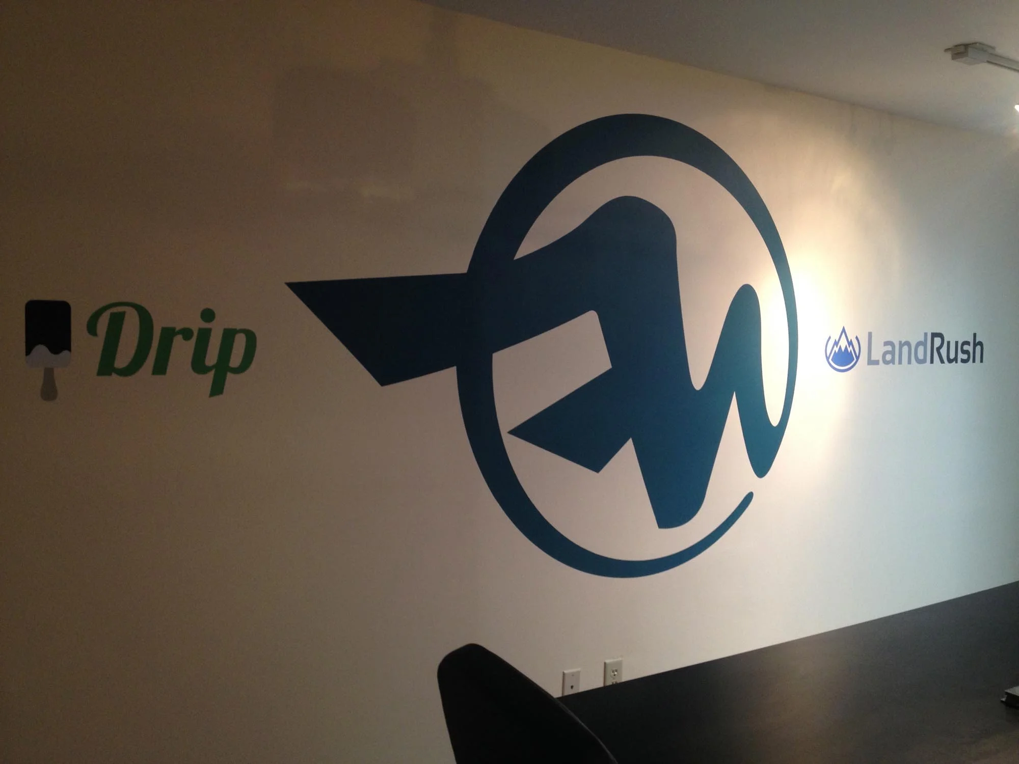 Wall with logos for 'Drip' and 'LandRush'; the 'Drip' logo has a black and white icon resembling a drip, and the 'LandRush' logo has blue text and a mountain icon.