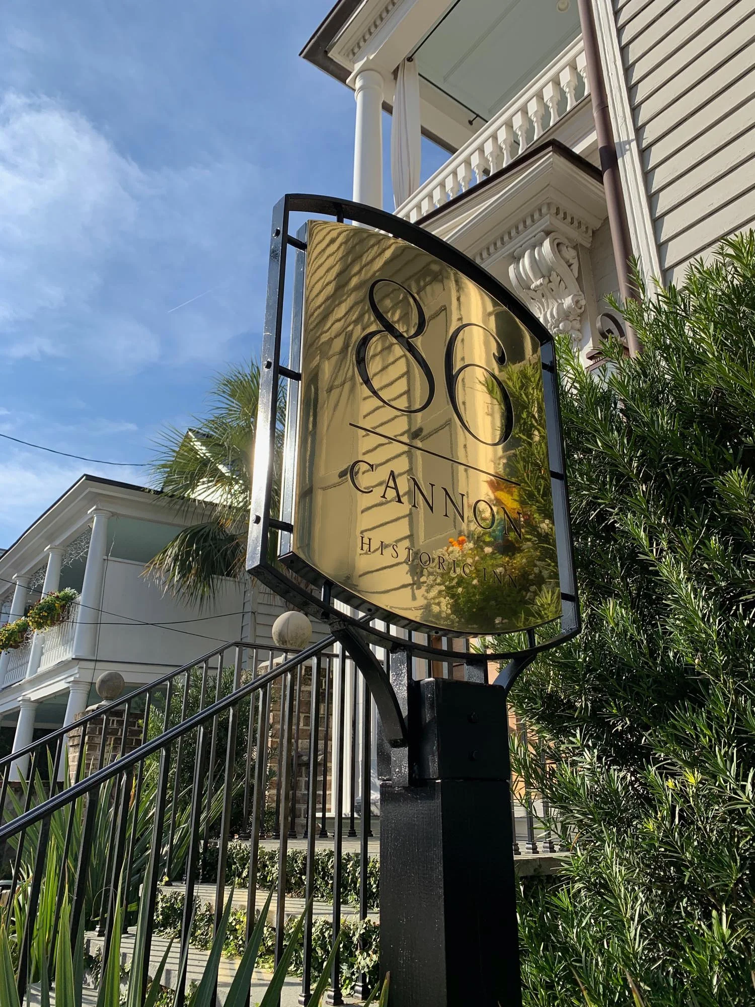 Golden sign with black lettering reading '86 Cannon Historic Inn' in front of a white Victorian style house with porches and balconies, surrounded by greenery under a blue sky.