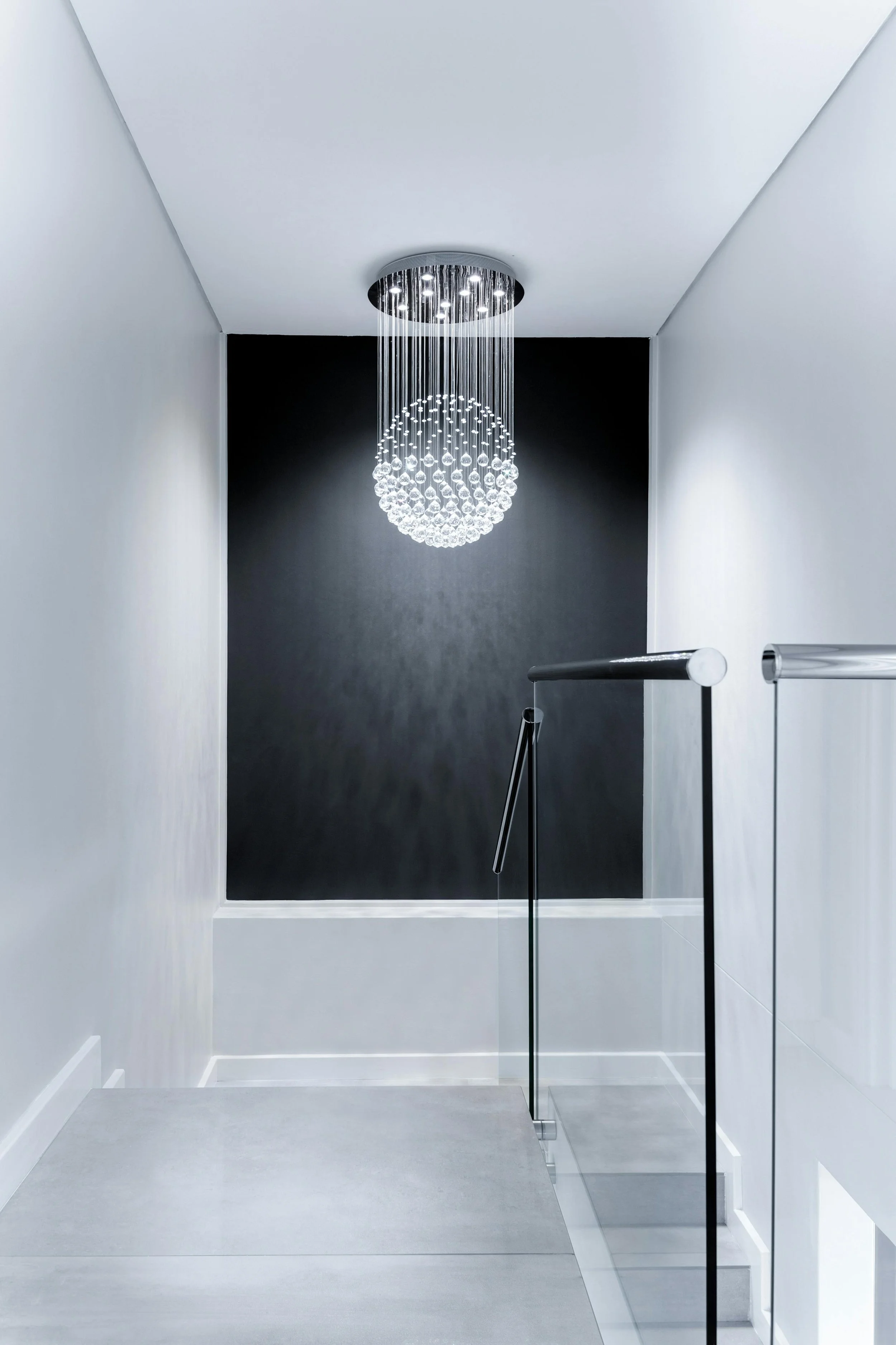 Modern stairway landing with a contemporary chandelier hanging from the ceiling, black accent wall, white walls, and glass railing.
