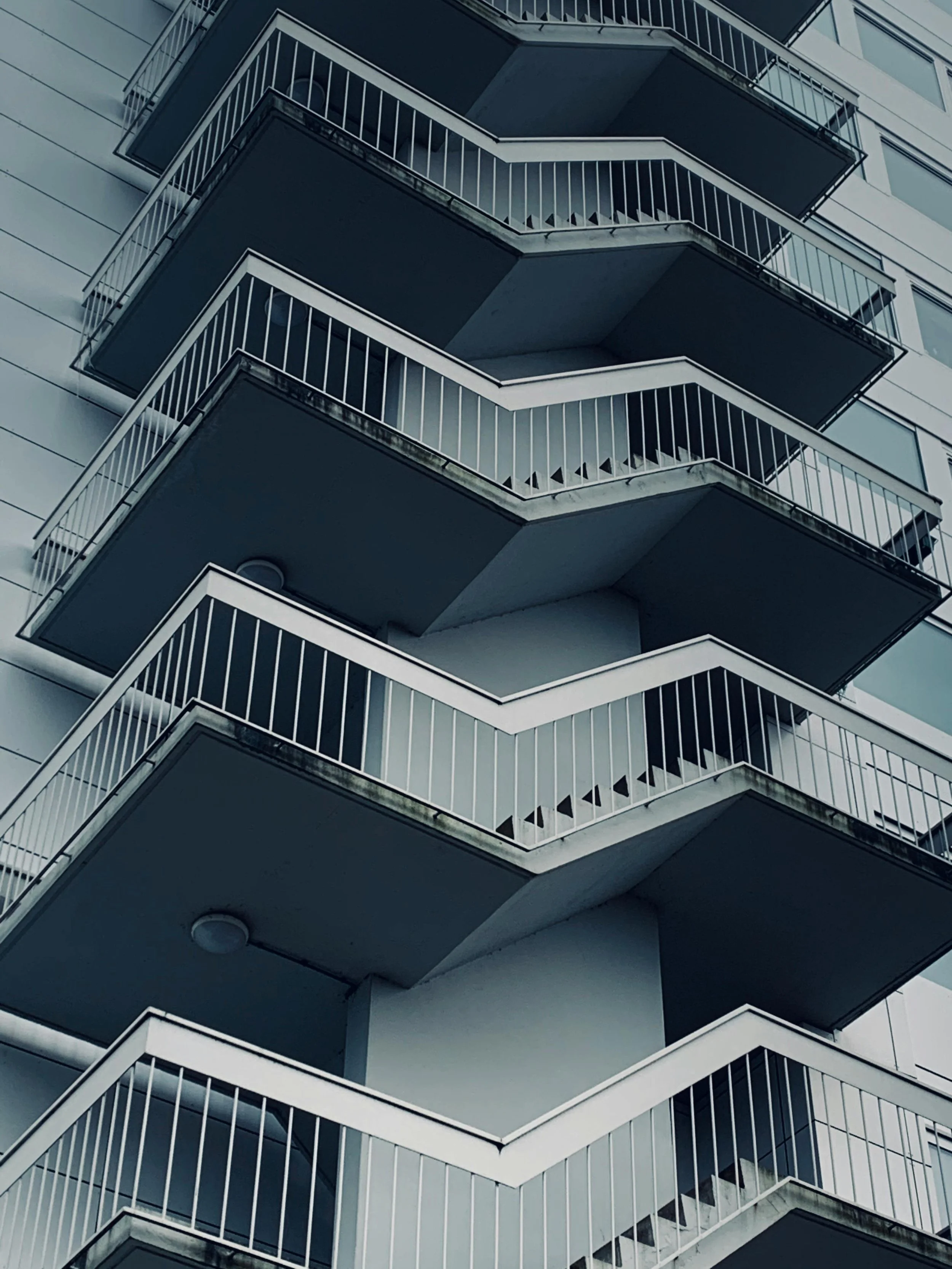 Multiple stacked balconies with white railings on a modern building, viewed from below.