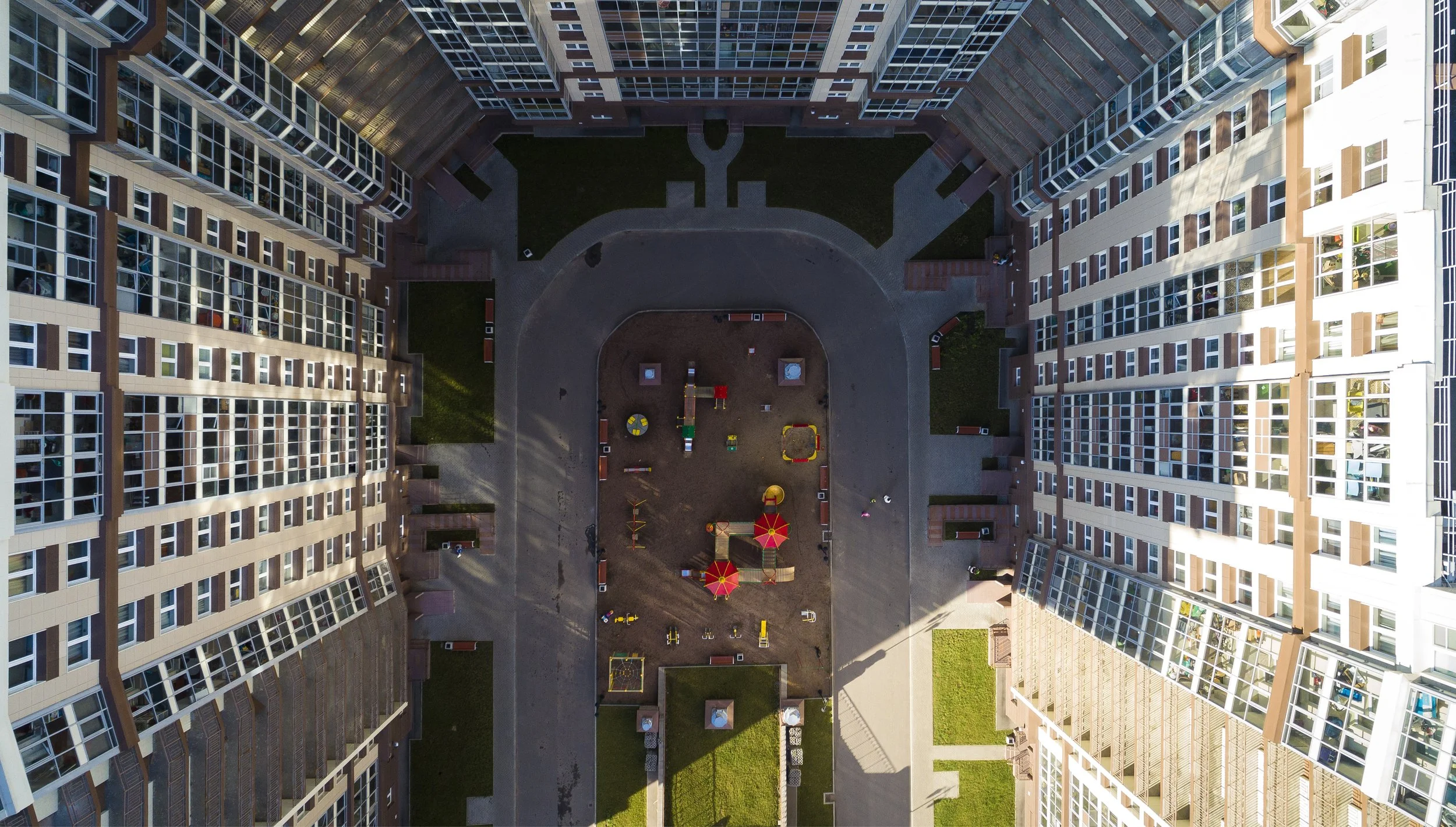A bird's eye view of a residential apartment complex courtyard with playground equipment, benches, and green lawns.