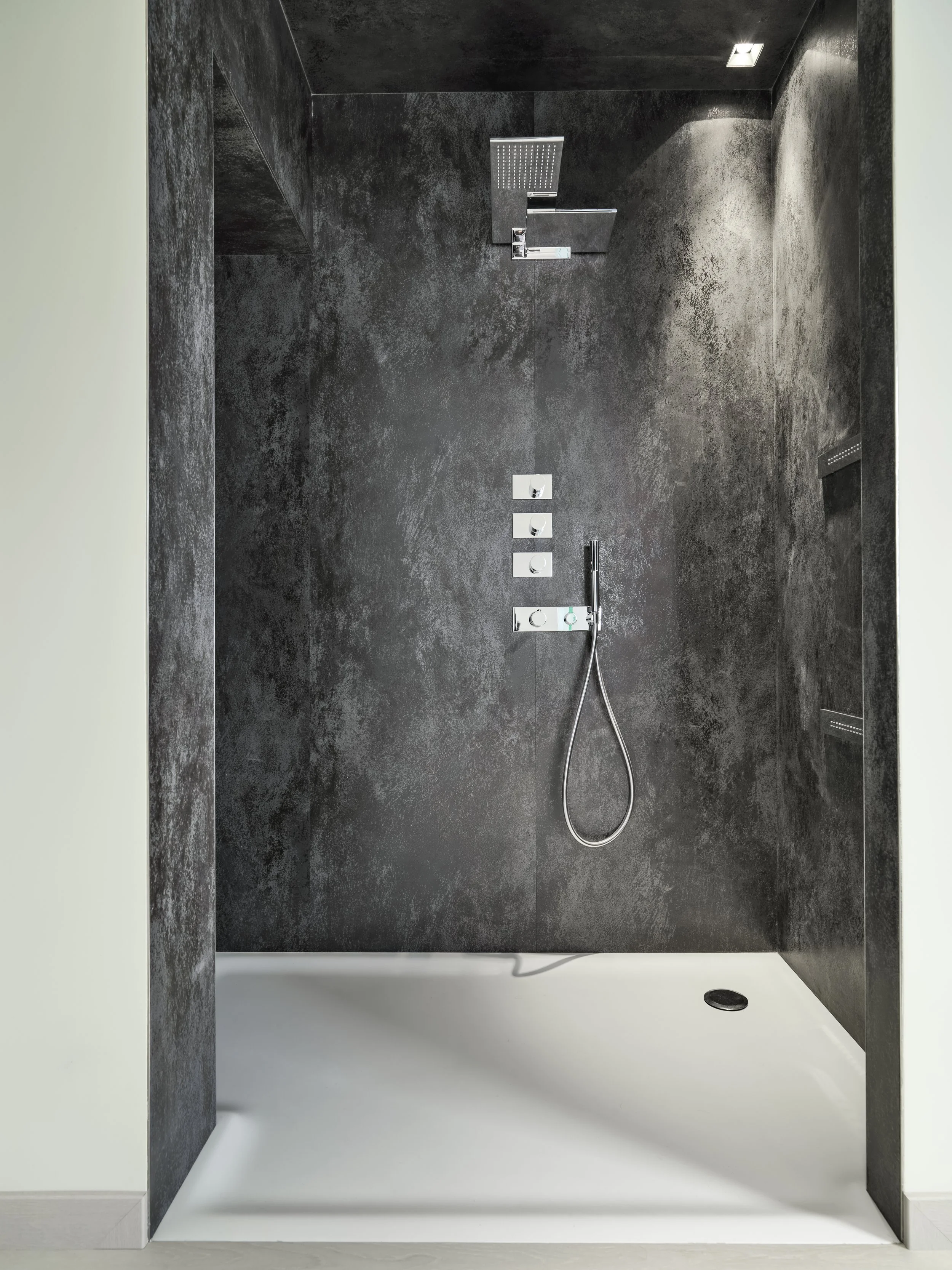 Modern walk-in shower with black textured walls, a rain showerhead, a handheld shower, and multiple controls, with a white shower tray.