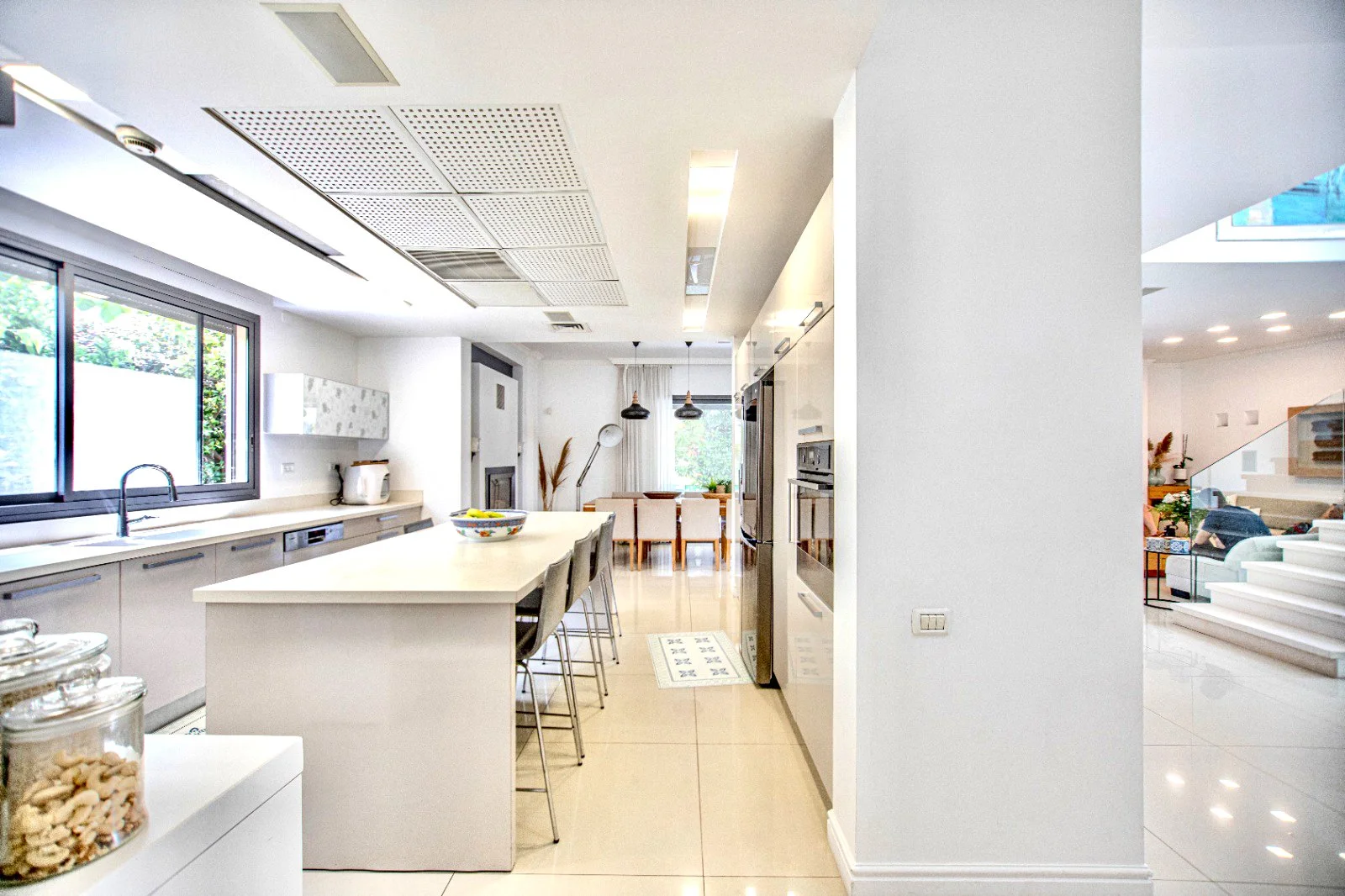 Modern open-concept kitchen with white cabinets, a large island, bar stools, stainless steel appliances, and a dining area with a table and chairs in the background.