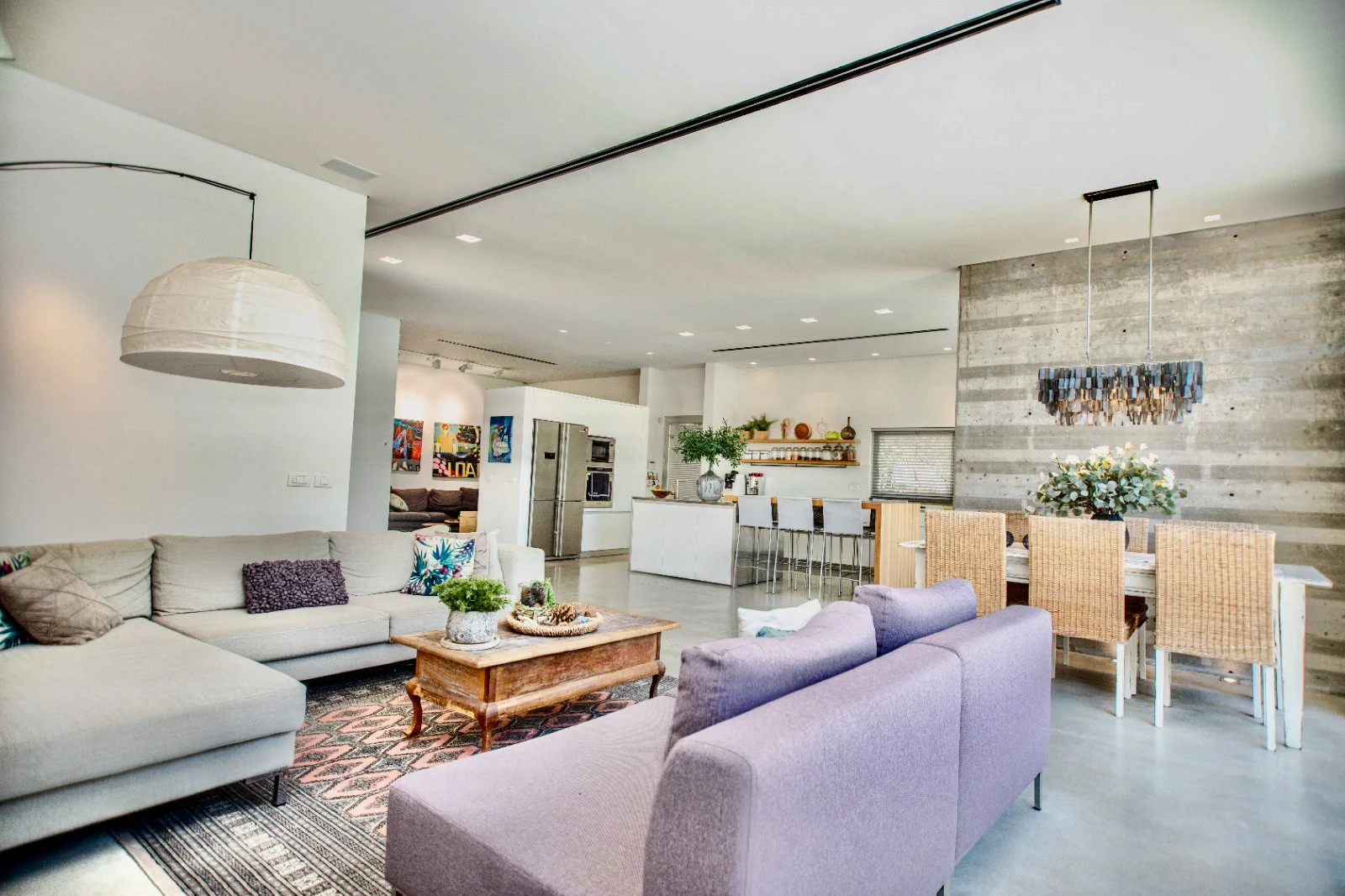 Open-concept living and dining area with modern furniture, a kitchen island with barstools, floral arrangements, and a concrete accent wall.