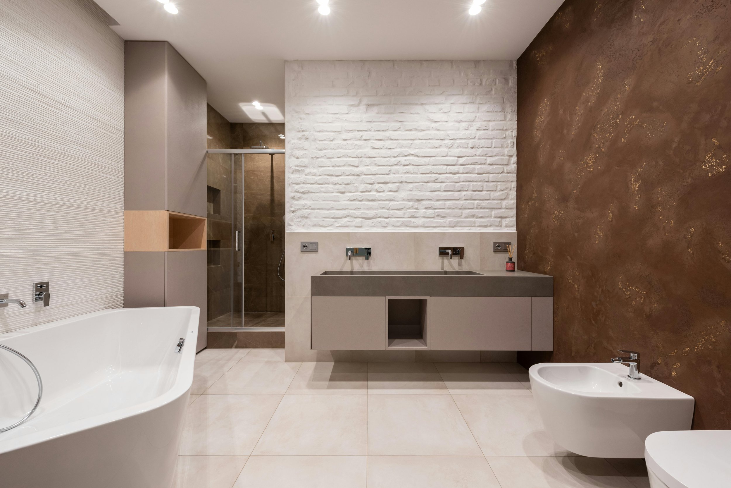 Modern bathroom with a bathtub, shower, double sink vanity, bidet, and textured walls in white, brown, and gray tones.
