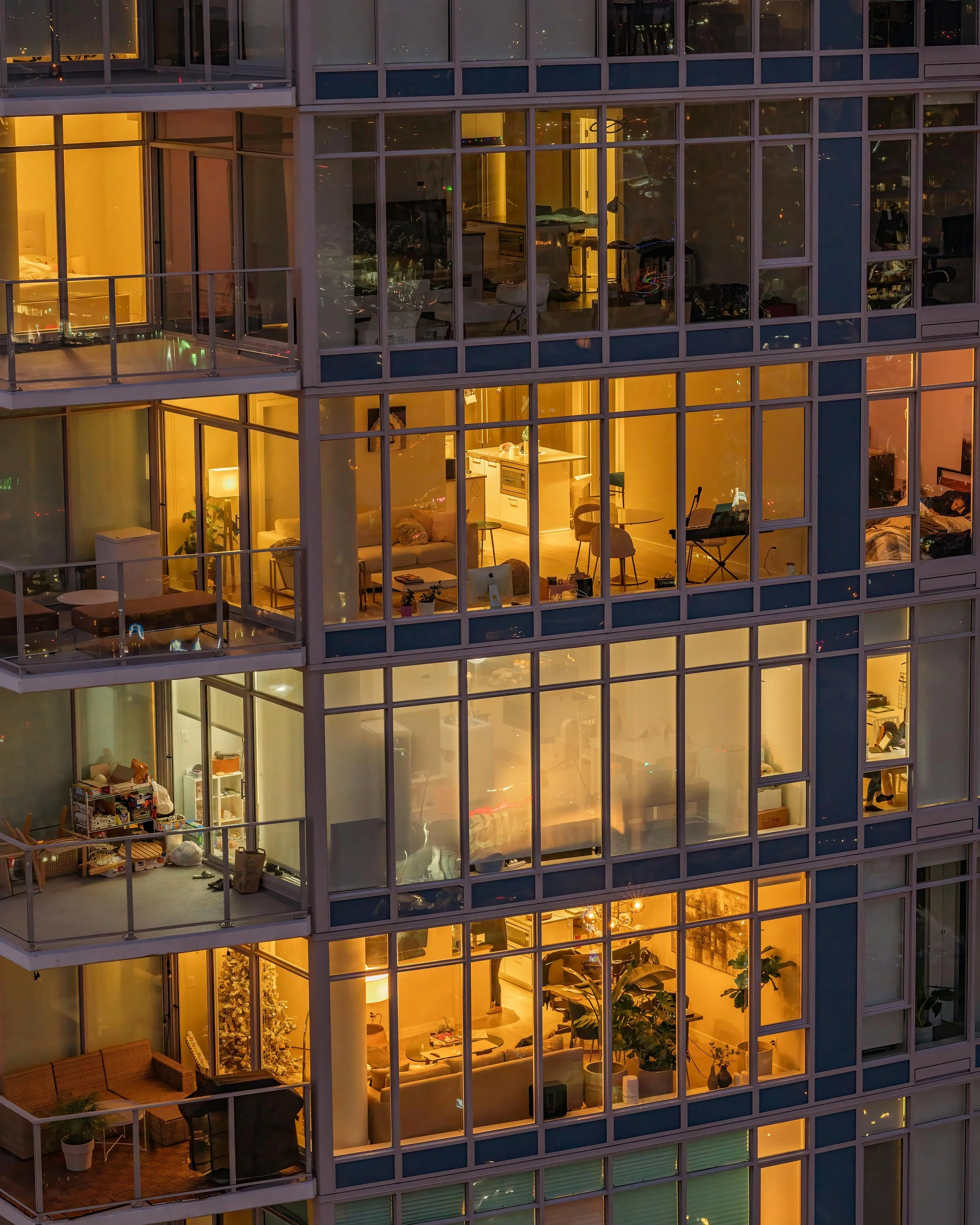 Multiple residential apartments in a high-rise building at night, with lit interior rooms visible through large glass windows.