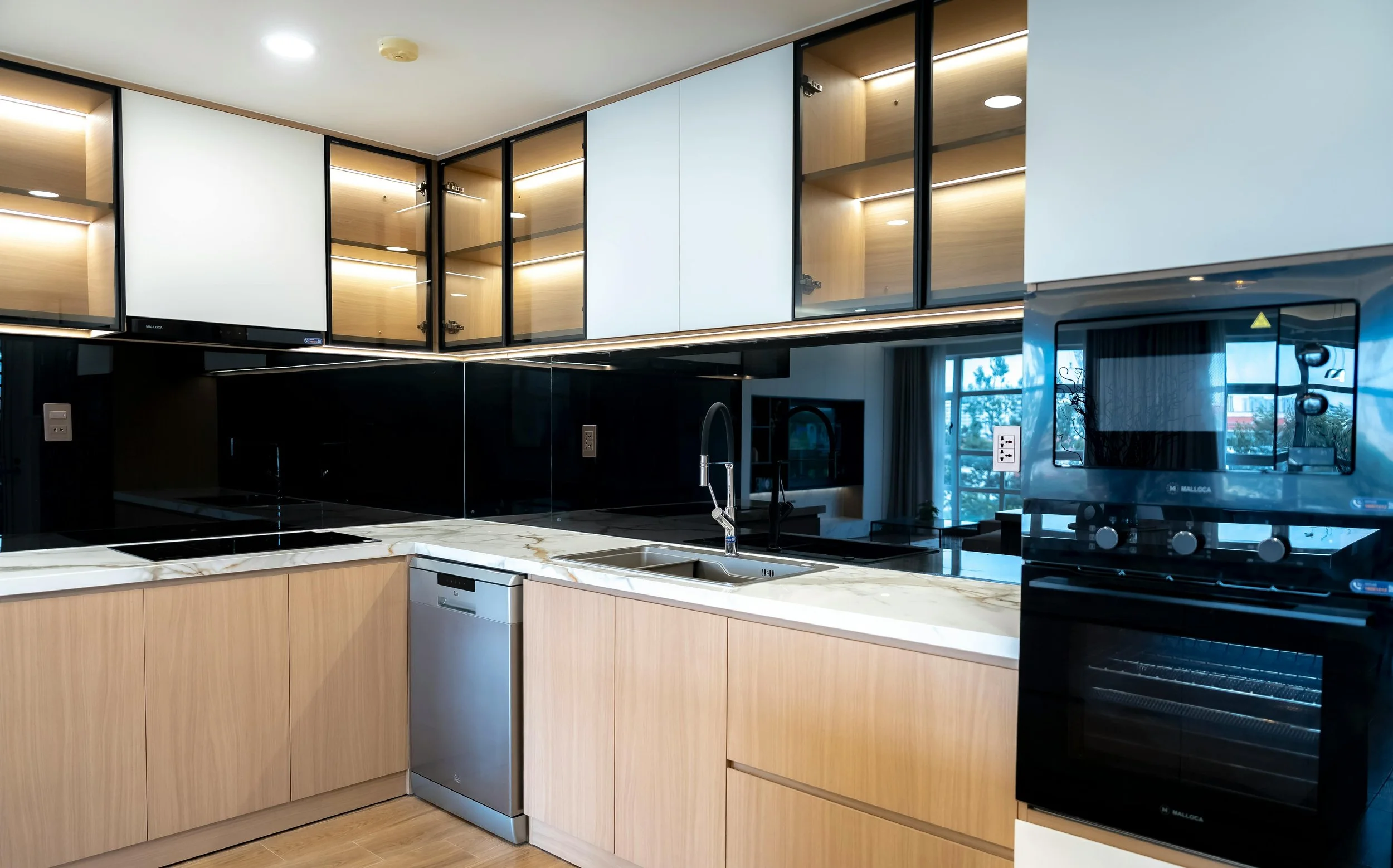 Modern kitchen with wooden cabinets, marble countertop, black glass backsplash, stainless steel appliances, and upper cabinets with glass doors and interior lighting.