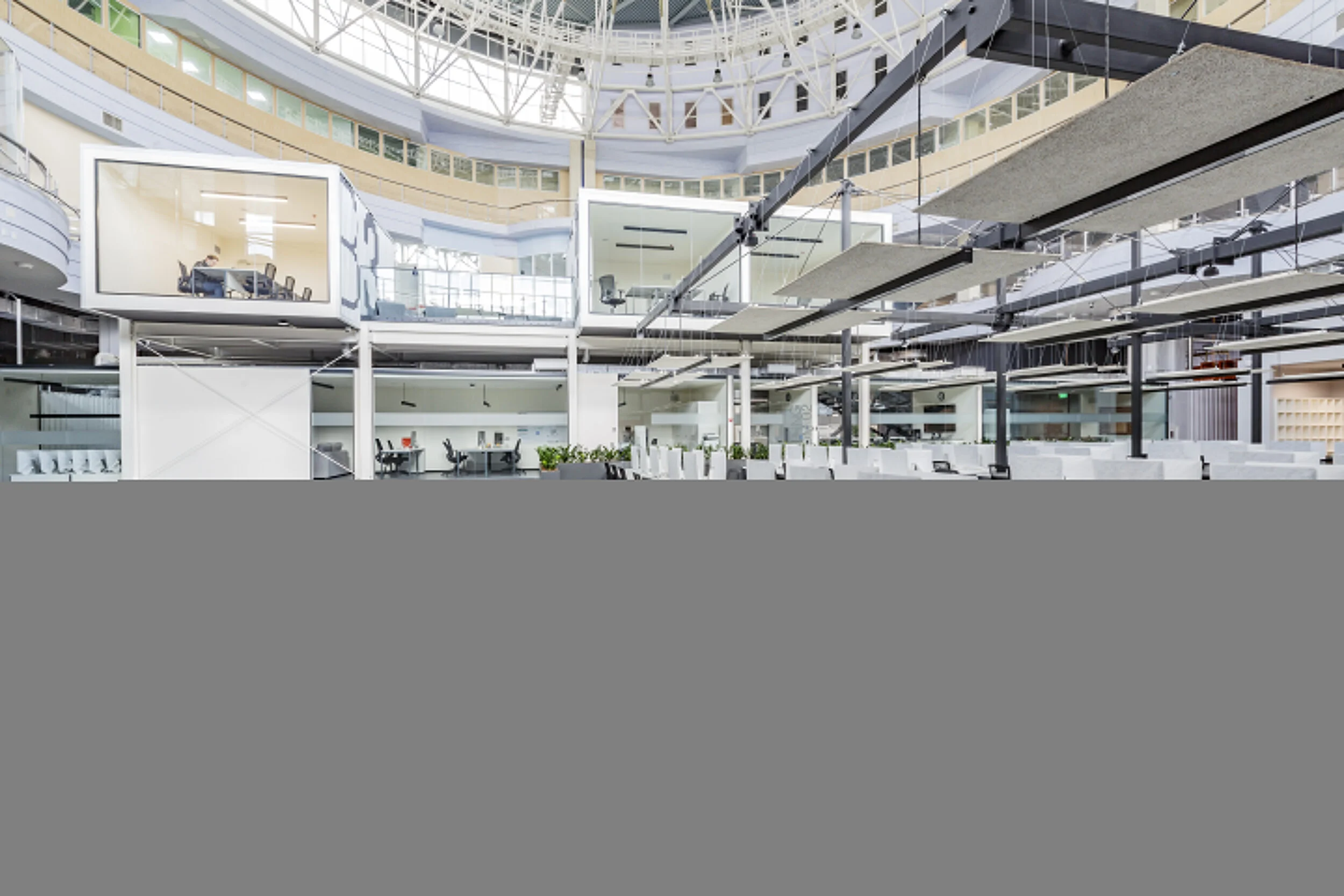 Modern multi-story office building with open office layout, glass-walled conference rooms, and various workstations visible inside.