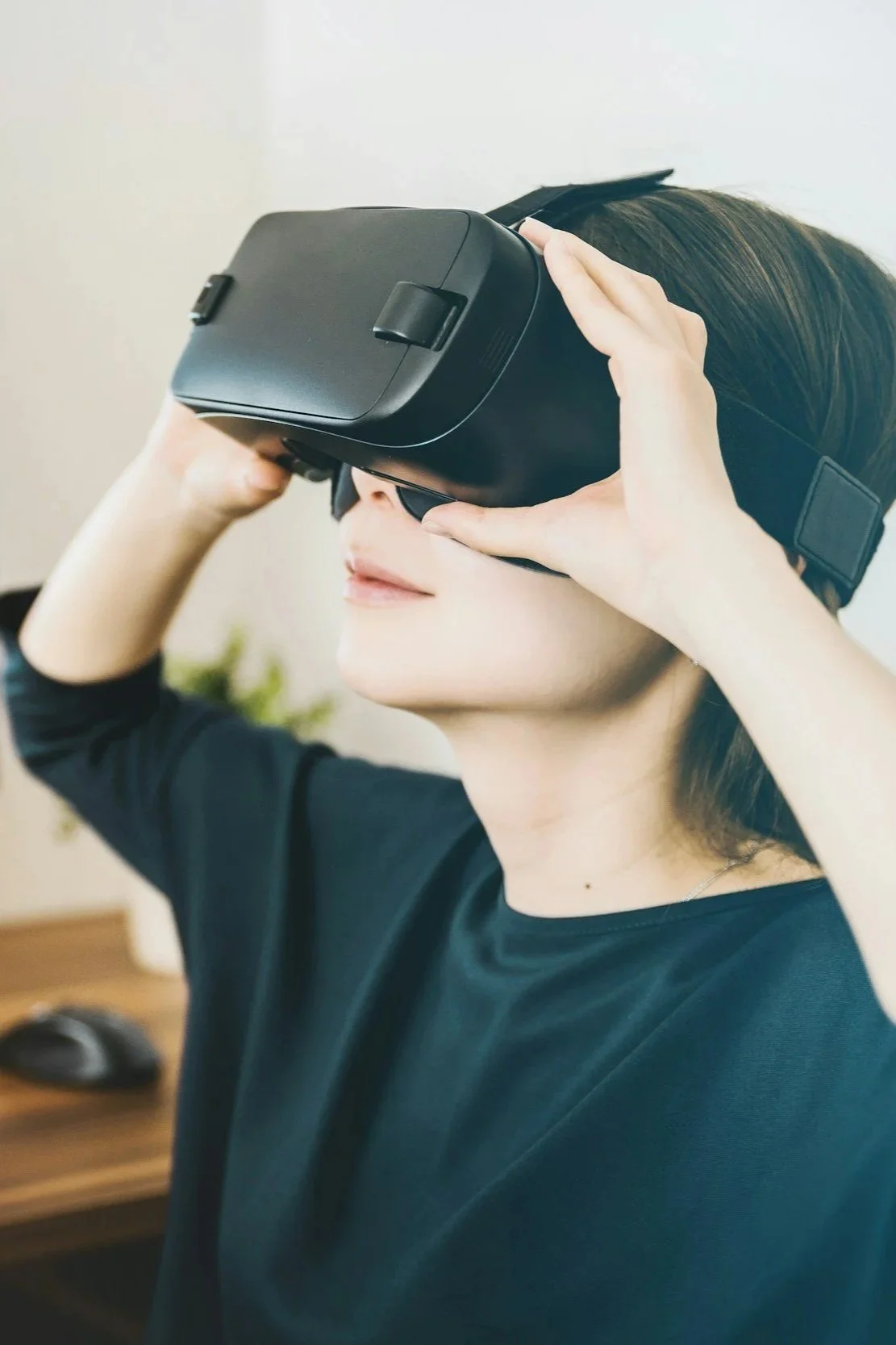 A woman wearing a black shirt using a virtual reality headset in a room with a blurred background.