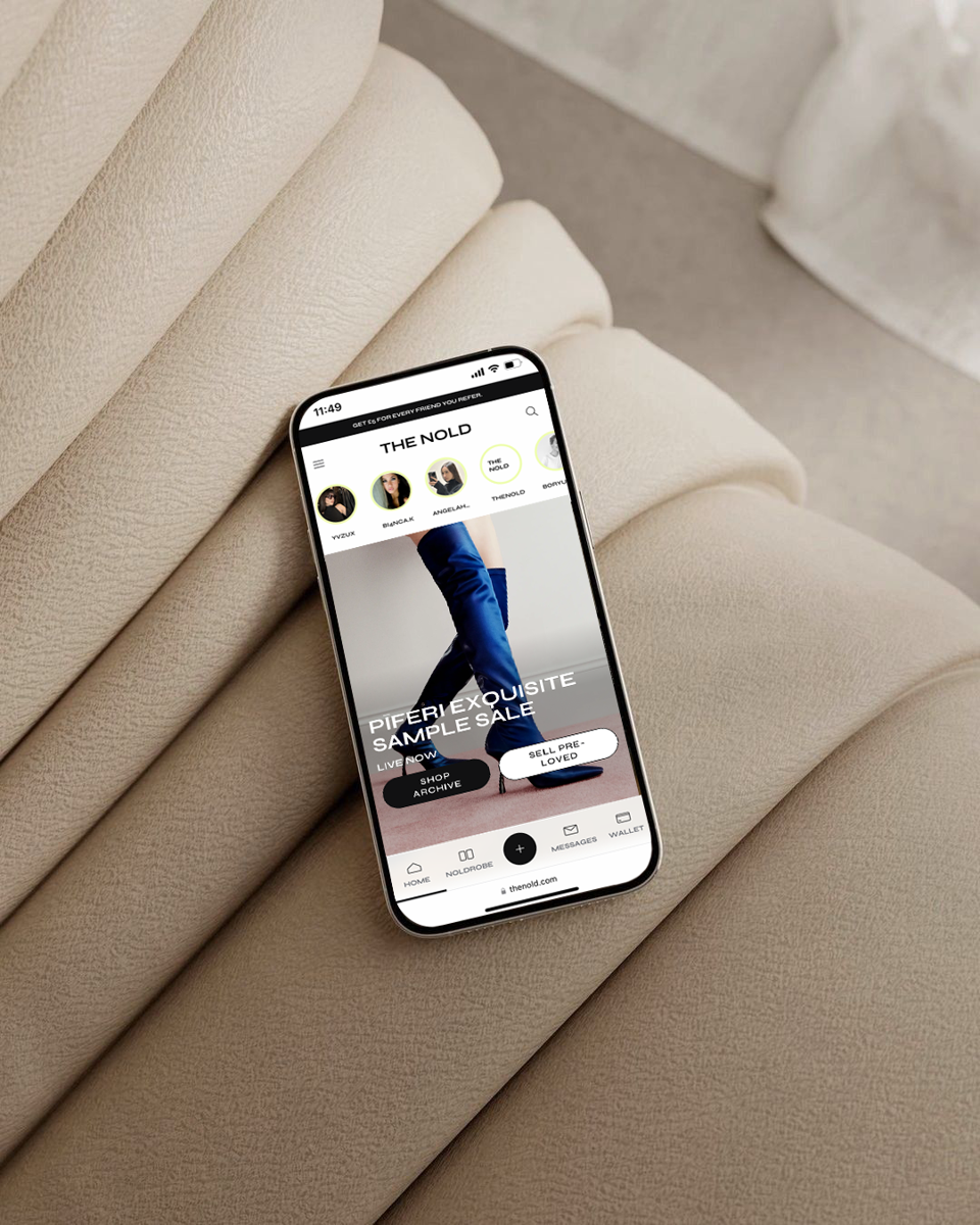 Smartphone displaying a fashion website, resting on a beige cushioned surface.