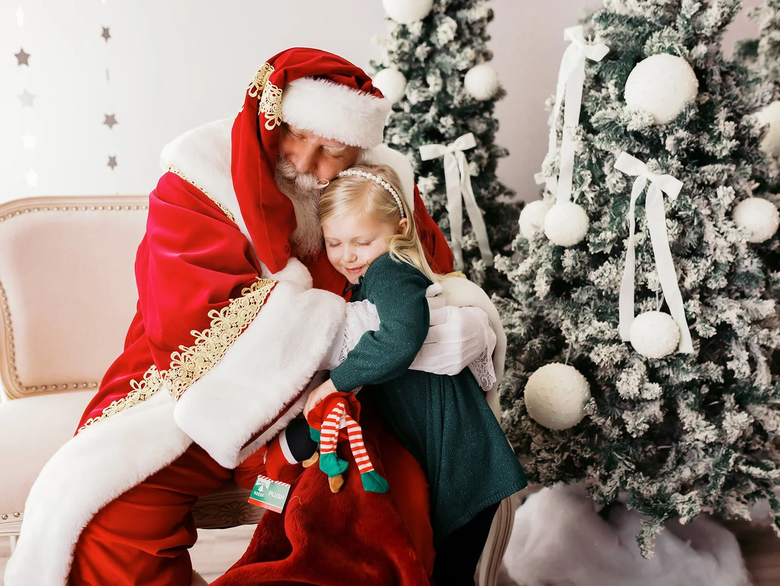 Santa Claus hugging a young girl in front of decorated Christmas trees.