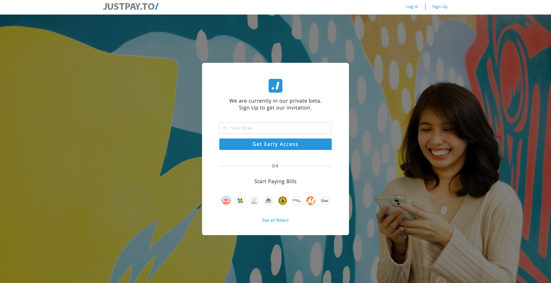 A young woman with dark hair smiling and looking at her phone in front of colorful graffiti art on a wall.