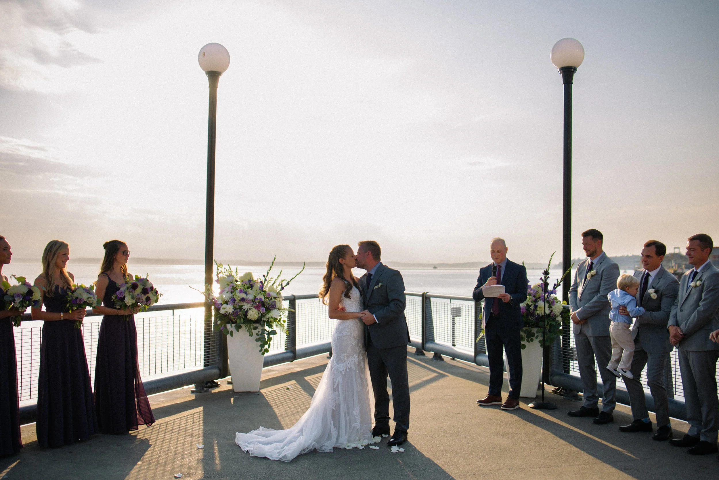 First kiss during outdoor waterfront wedding ceremony on the Seattle waterfront near the Seattle Aquarium.