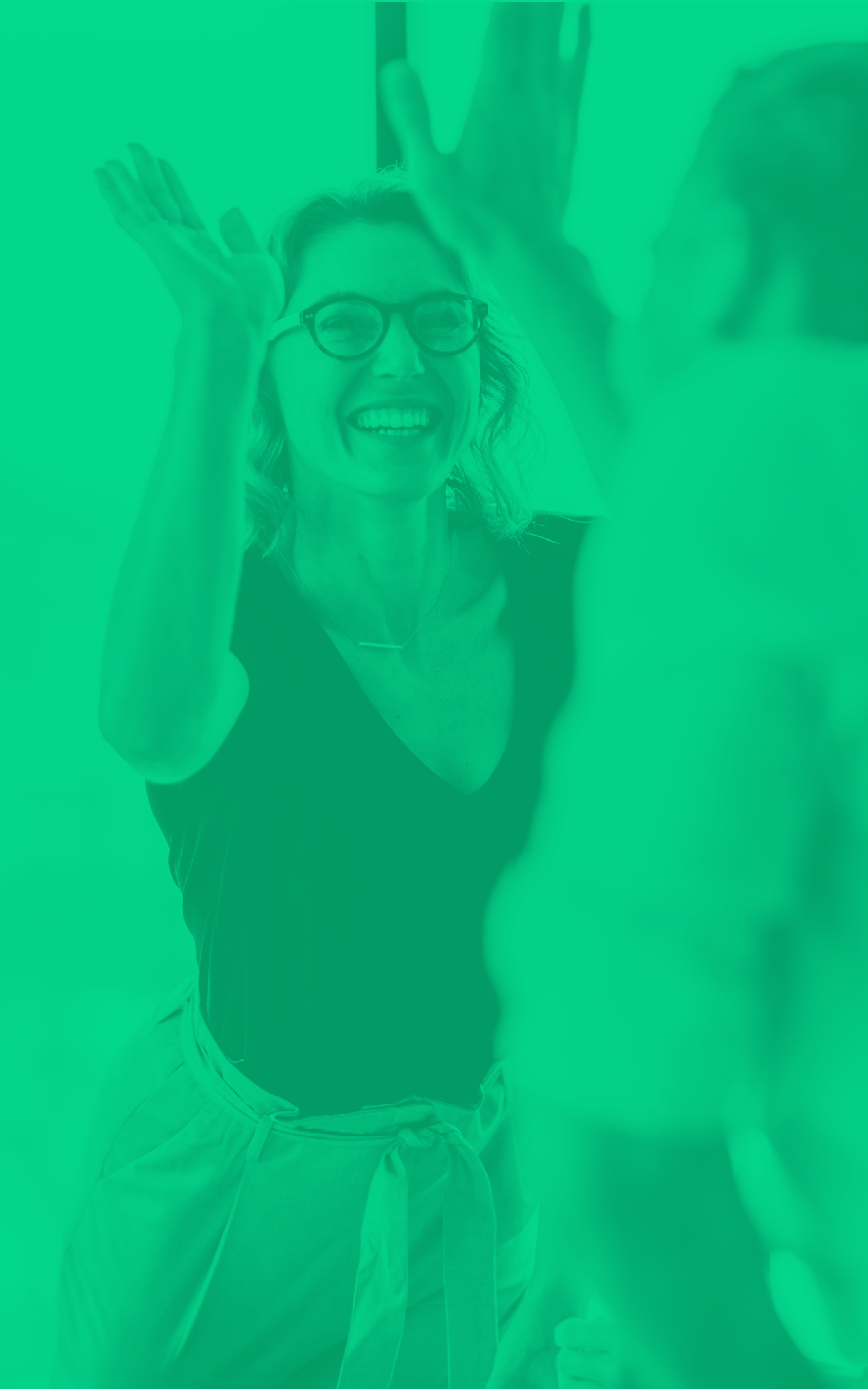 A woman with glasses smiling and raising her hands in greeting.