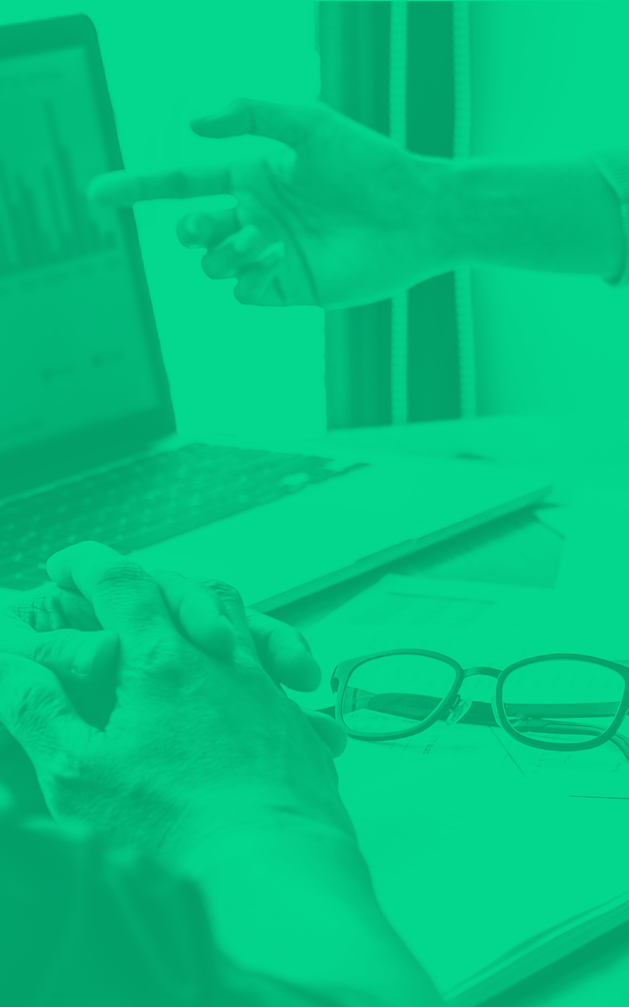 A person's hand holding a smartphone, sitting at a desk with a laptop, a pair of glasses, and a pair of reading glasses nearby.